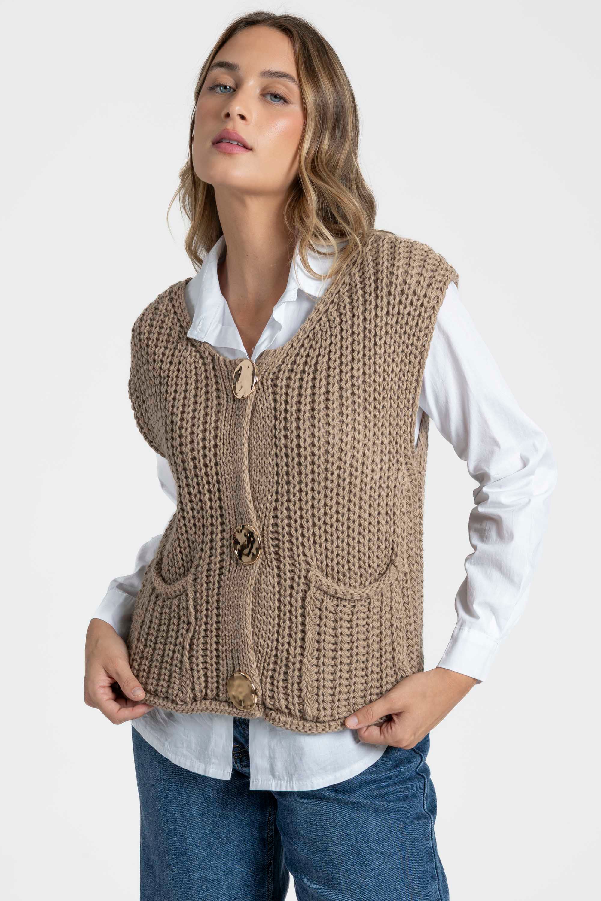 Femme portant un gilet sans manches en maille femme beige, avec boutons métalliques et détails élégants, associé à une chemise blanche. Gilet maille femme.