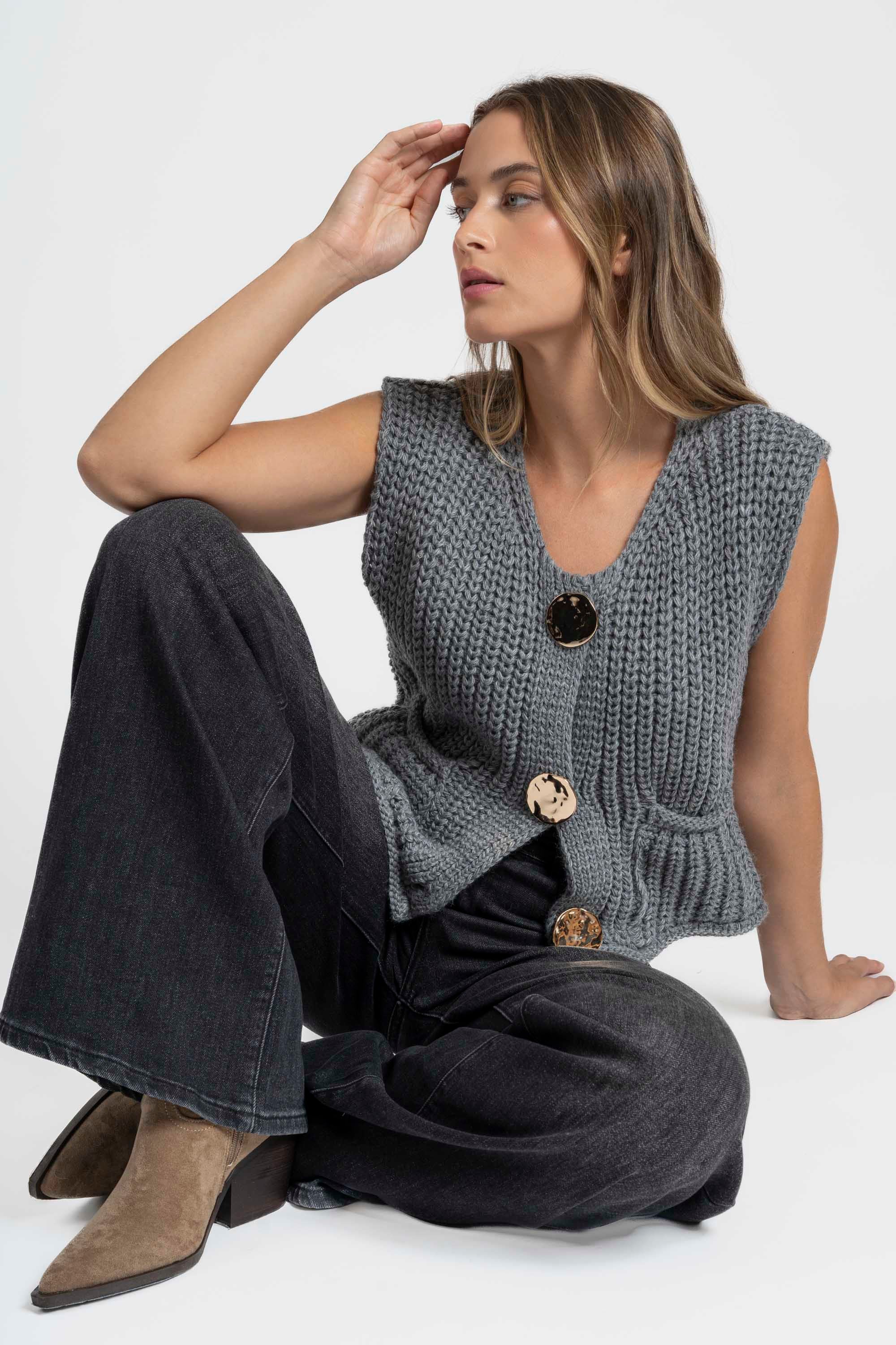 Modèle portant un gilet sans manches en maille femme, couleur grise, avec boutons métalliques et poches, parfait pour un look décontracté. Gilet maille femme.