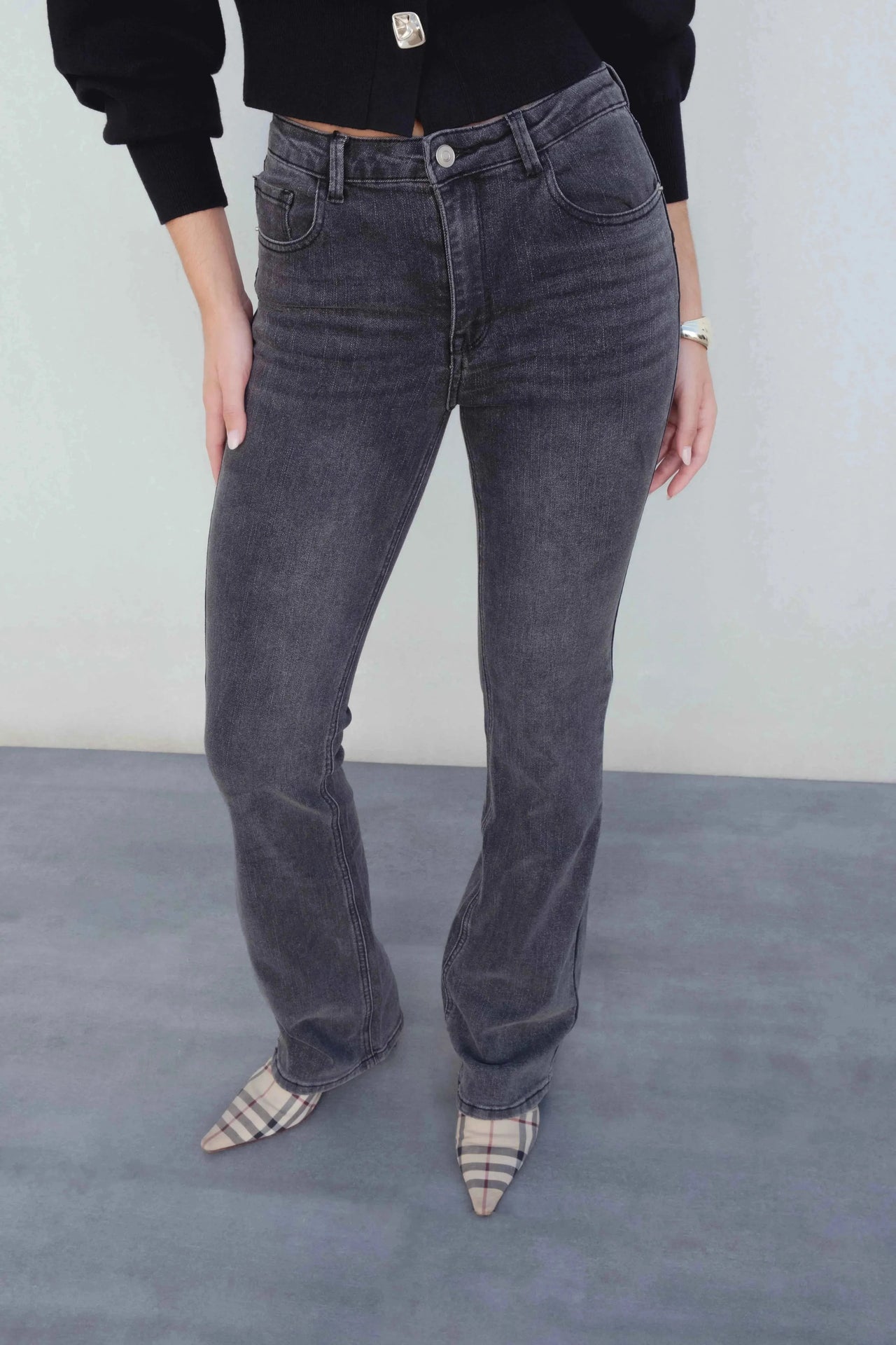 Présentation du jean femme gris évasé avec une blouse noire, accessoirisé avec des escarpins, parfait pour un outfit tendance.