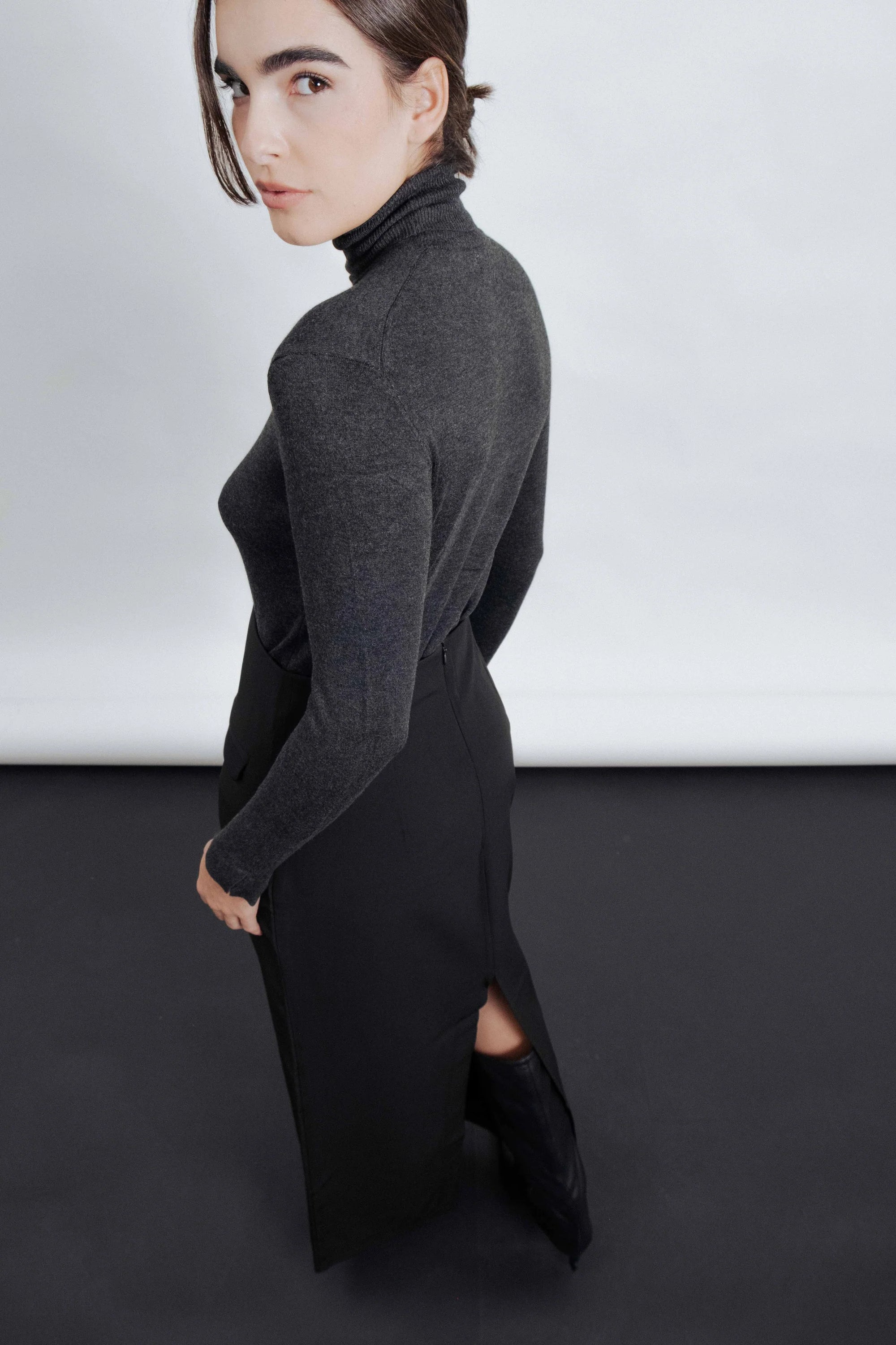 Femme posant en jupe midi noire avec fente latérale, mettant en valeur le style élégant et contemporain.