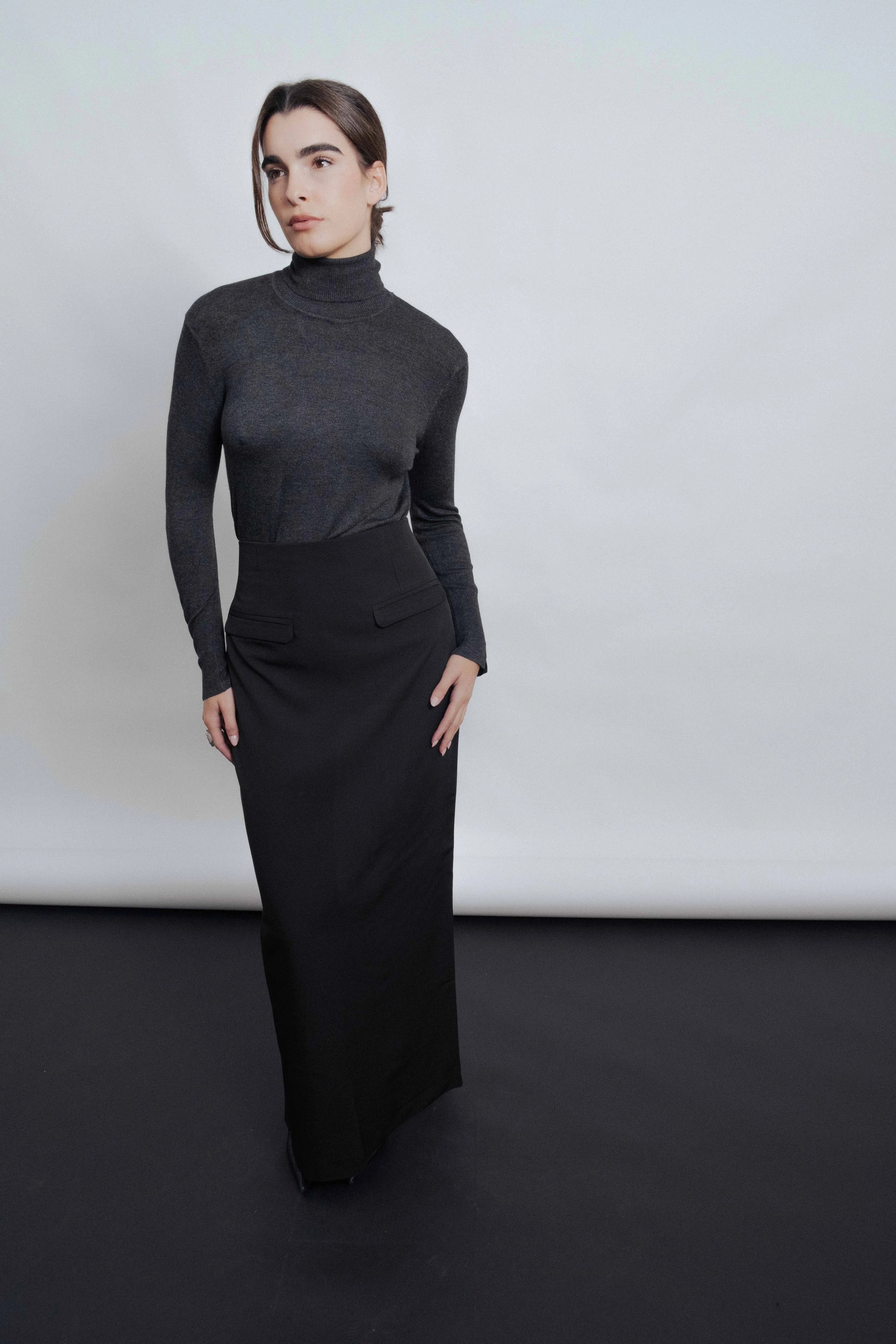 Modèle féminin affichant une jupe midi noire chic avec fente latérale, parfaite pour toutes les occasions.