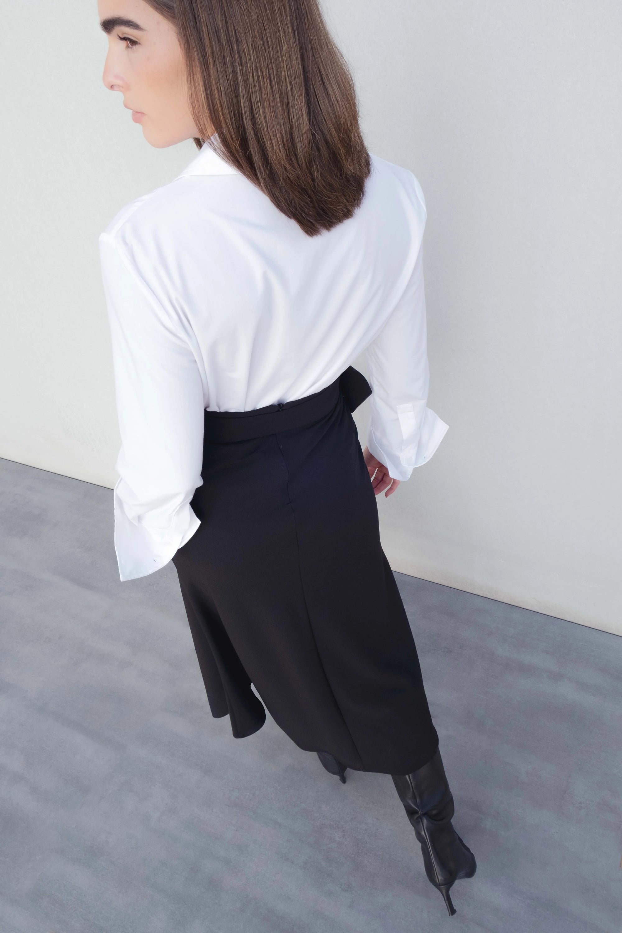 Vue arrière d'un modèle portant la jupe midi noire avec ceinture, mettant en lumière la coupe fluide et stylée.