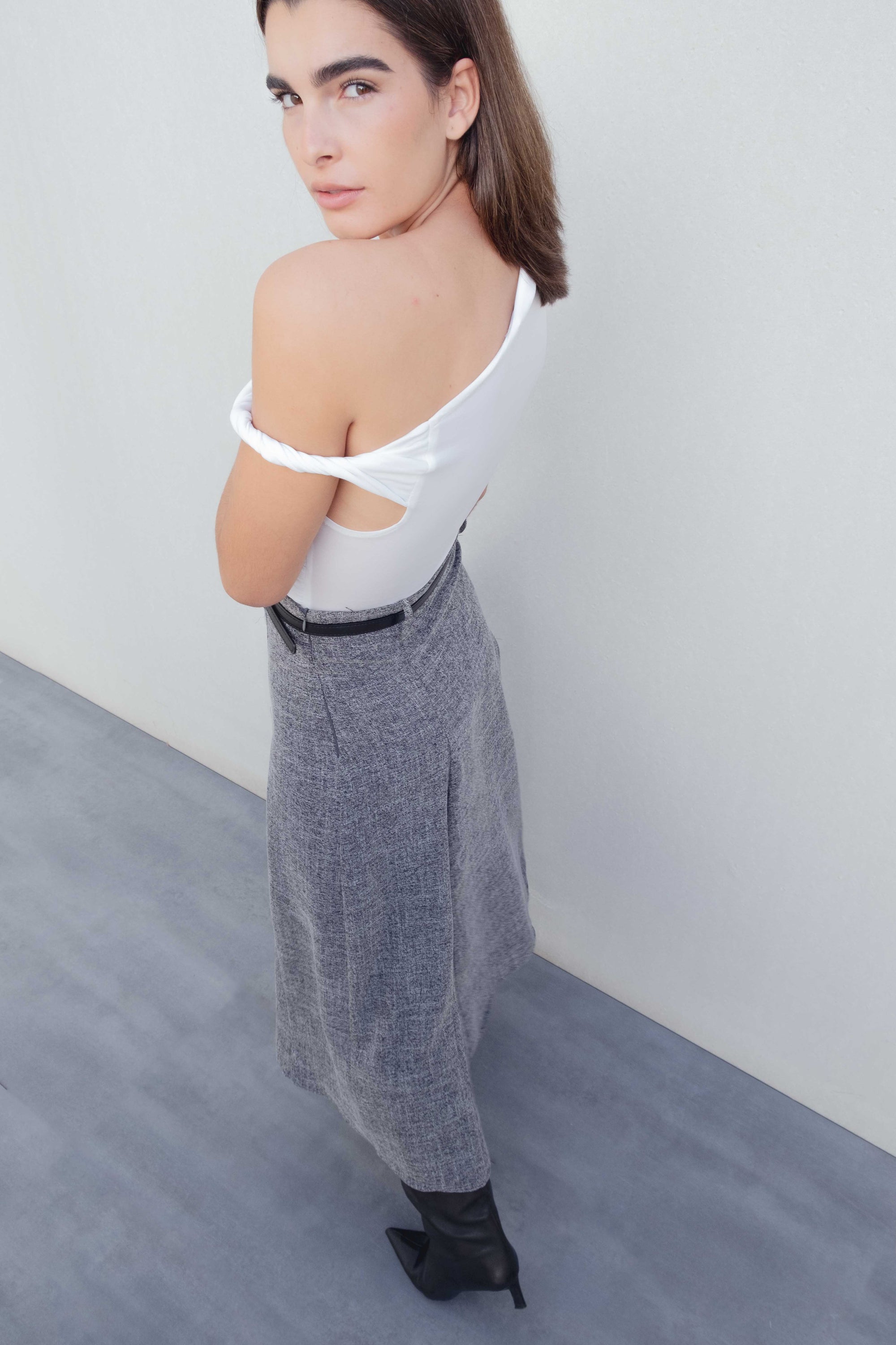 Femme portant une jupe midi structurée taille haute ceinture noire, en polyester et viscose, avec un top blanc. Cette jupe grise est parfaite pour un look élégant et moderne.