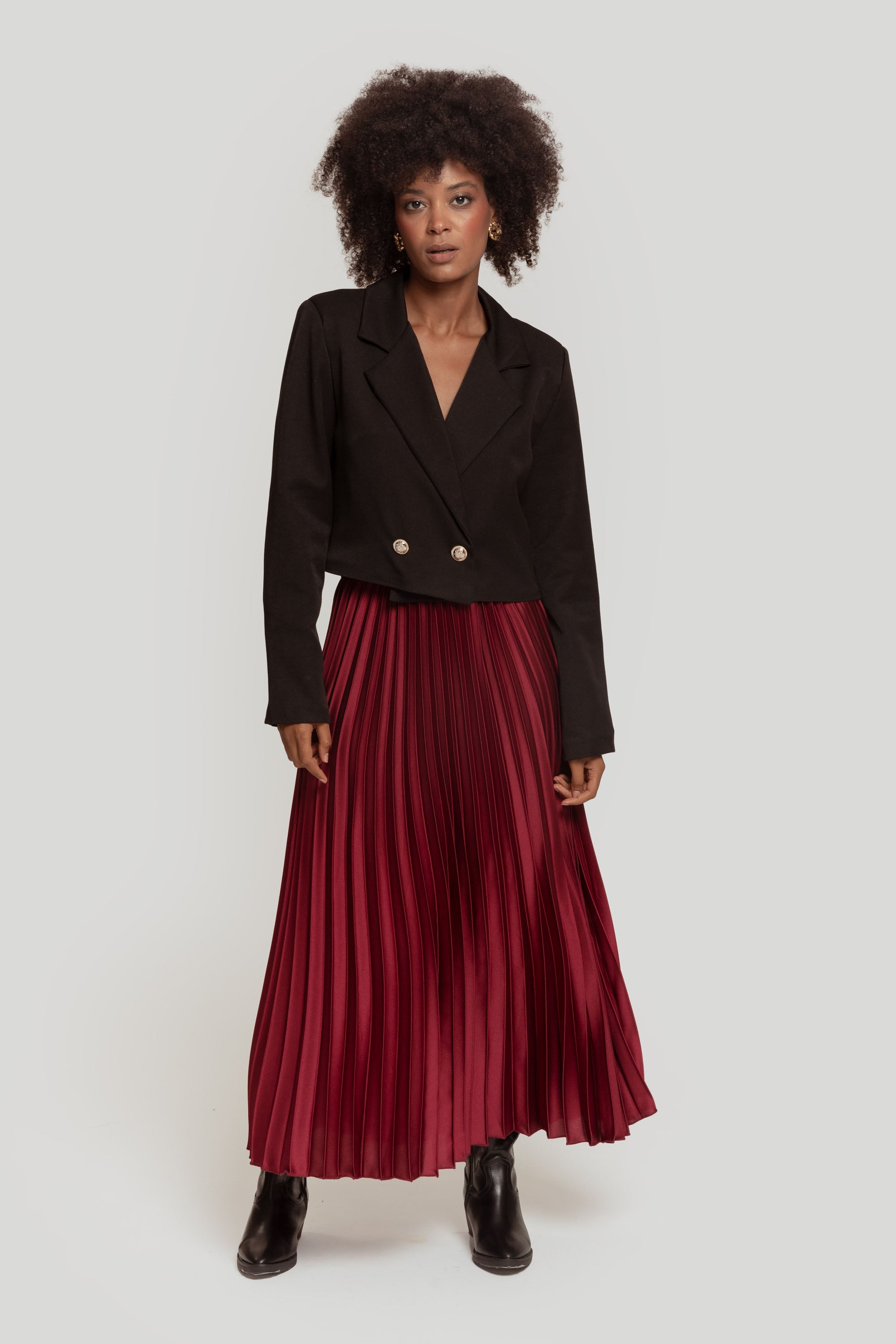 Femme portant une jupe midi plissée brillante taille haute de couleur bordeaux avec un blazer.