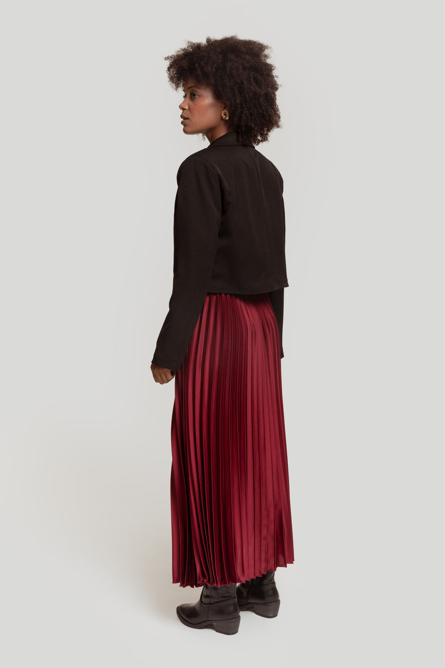 Vue de profil d'une femme en jupe midi plissée brillante taille haute bordeaux avec un look chic.