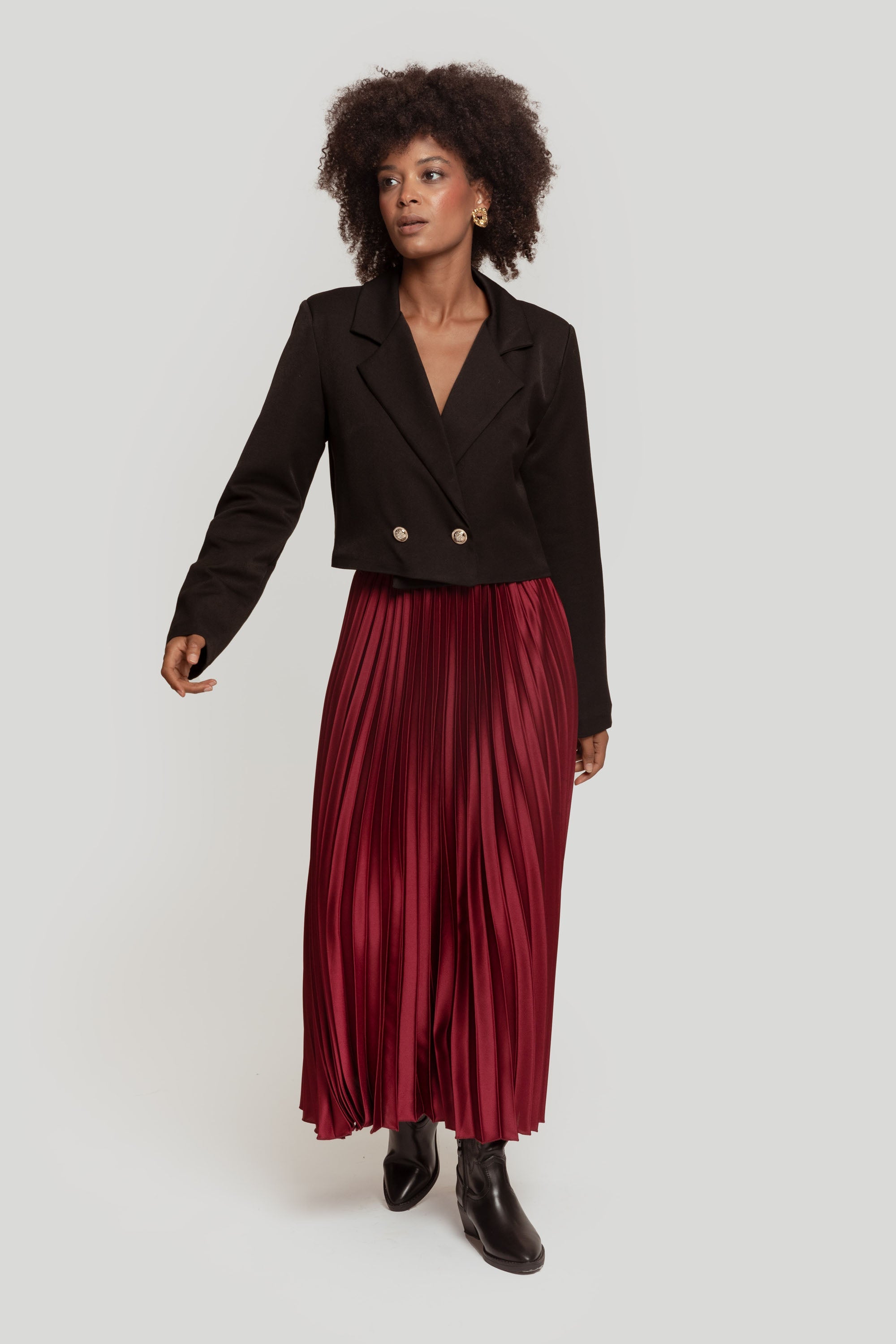 Femme souriante en jupe midi plissée brillante taille haute et blazer, une tenue polyvalente.