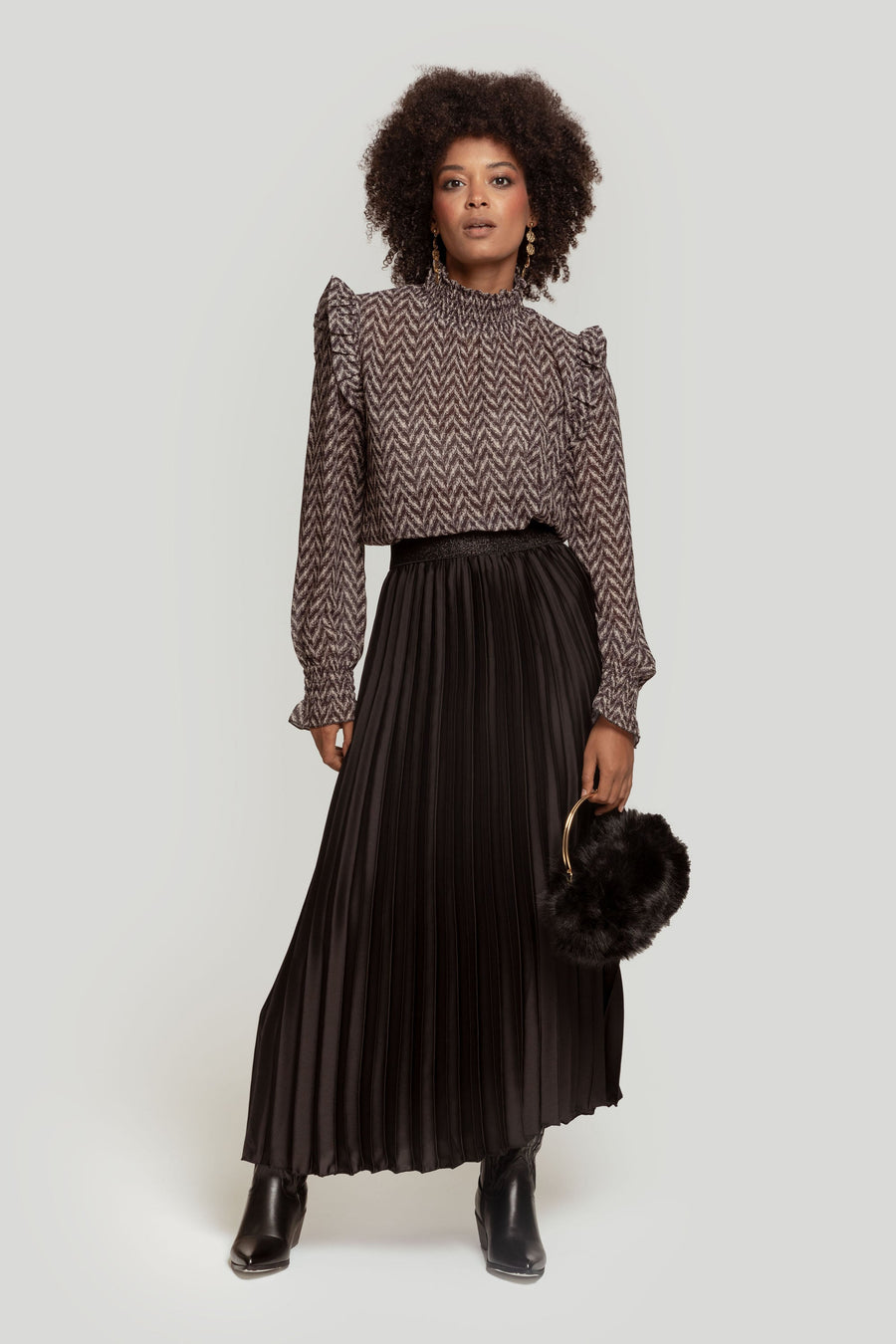 Femme portant une jupe midi plissée brillante taille haute avec une blouse à motifs, se tenait avec élégance.