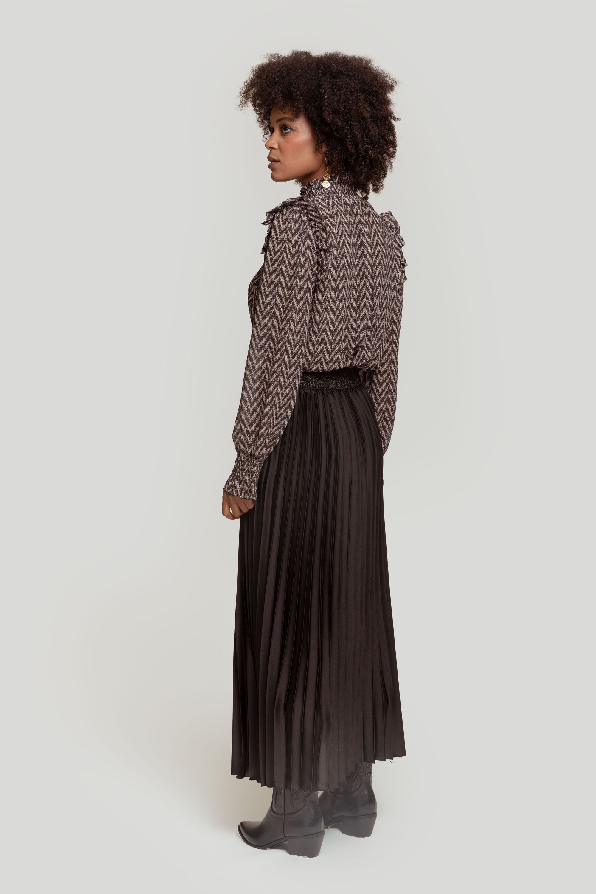 Vue de profil d'une femme en jupe midi plissée brillante taille haute, affichant un look moderne.