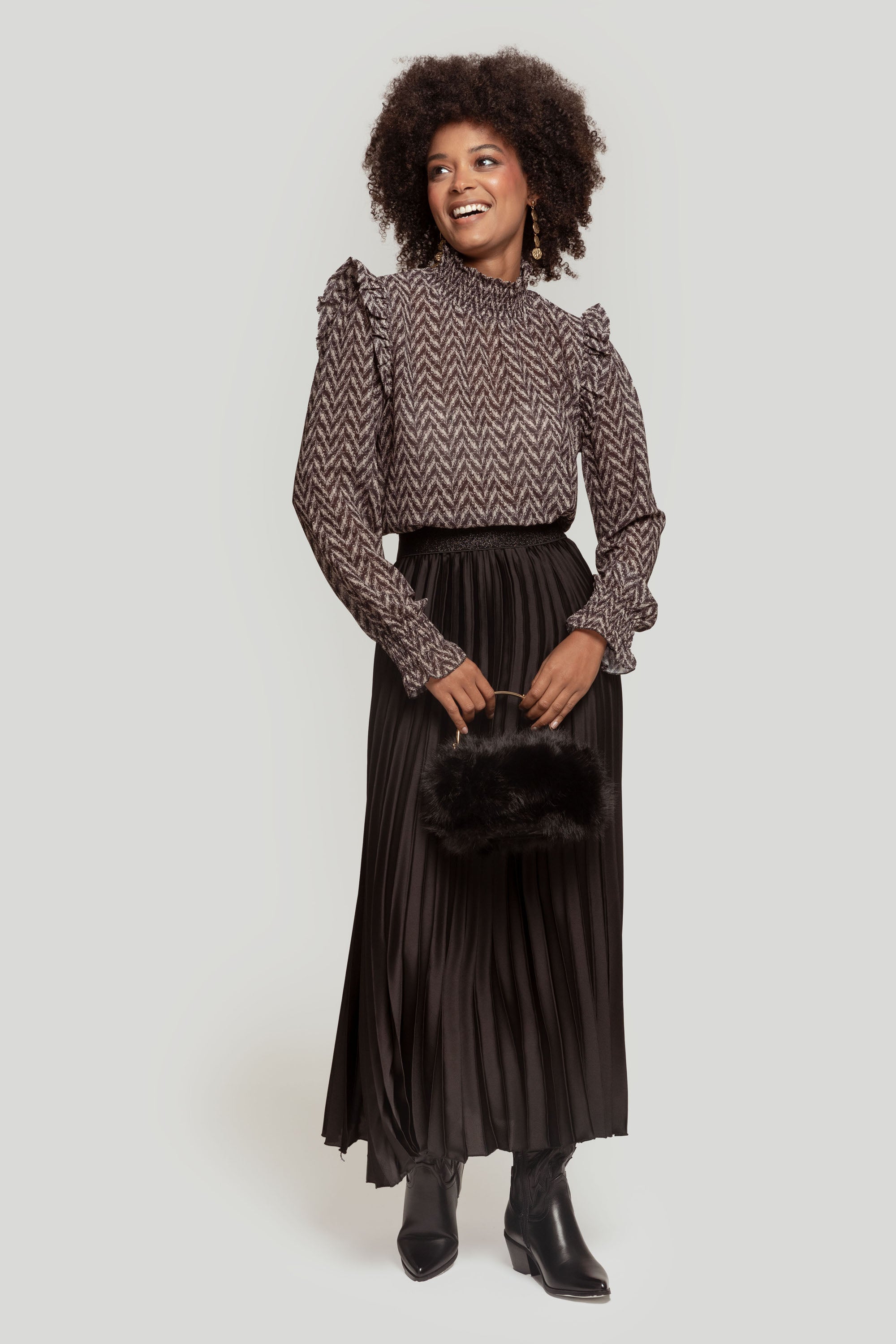 Femme souriante en jupe midi plissée brillante taille haute, combinaison chic avec une blouse à motifs.