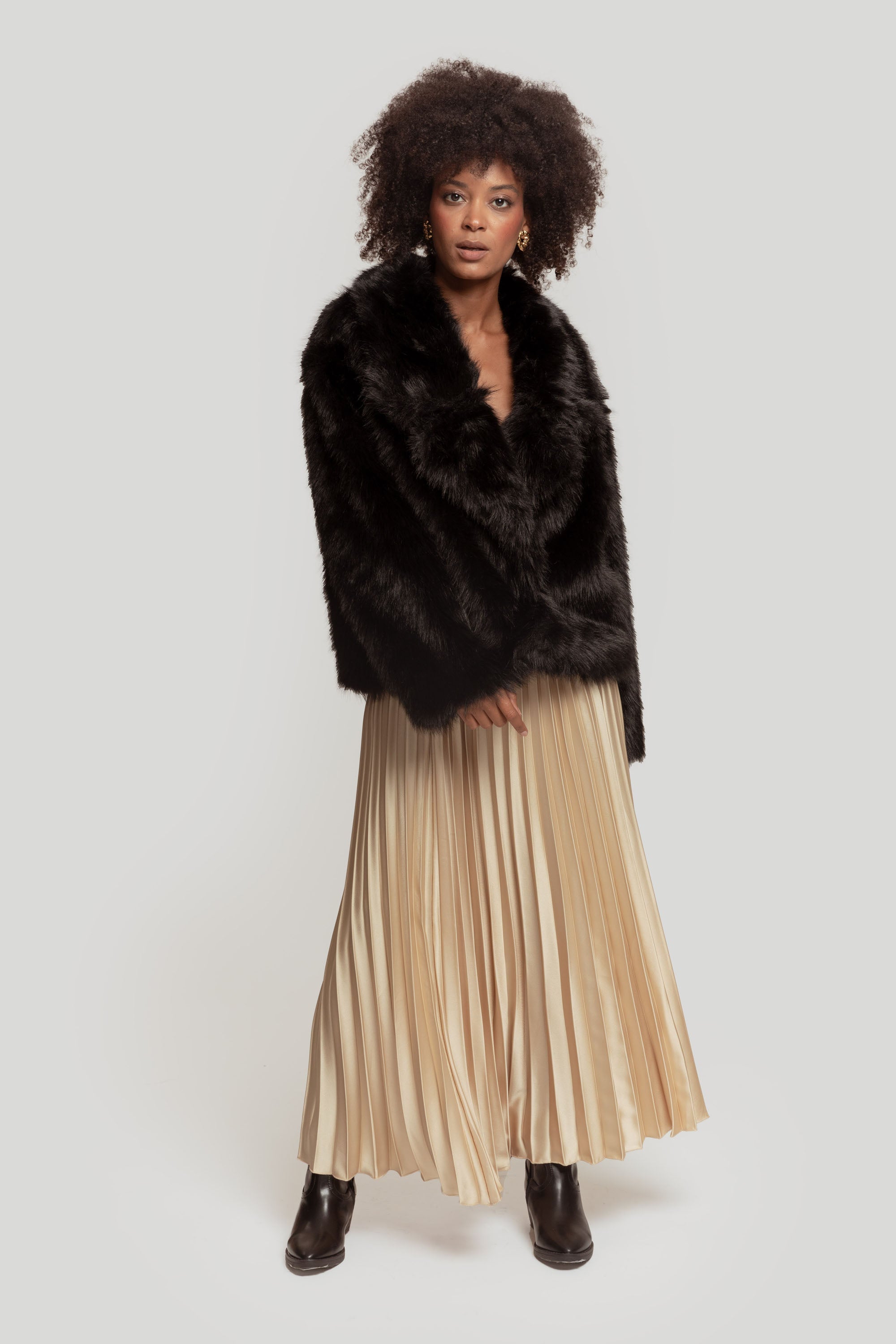 Femme avec une jupe midi plissée brillante taille haute de couleur beige portant un manteau en fausse fourrure.