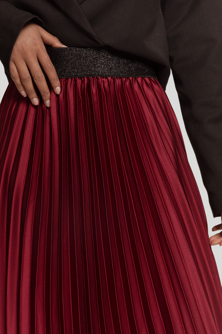 Gros plan sur la taille élastique d'une jupe midi plissée brillante taille haute couleur bordeaux.