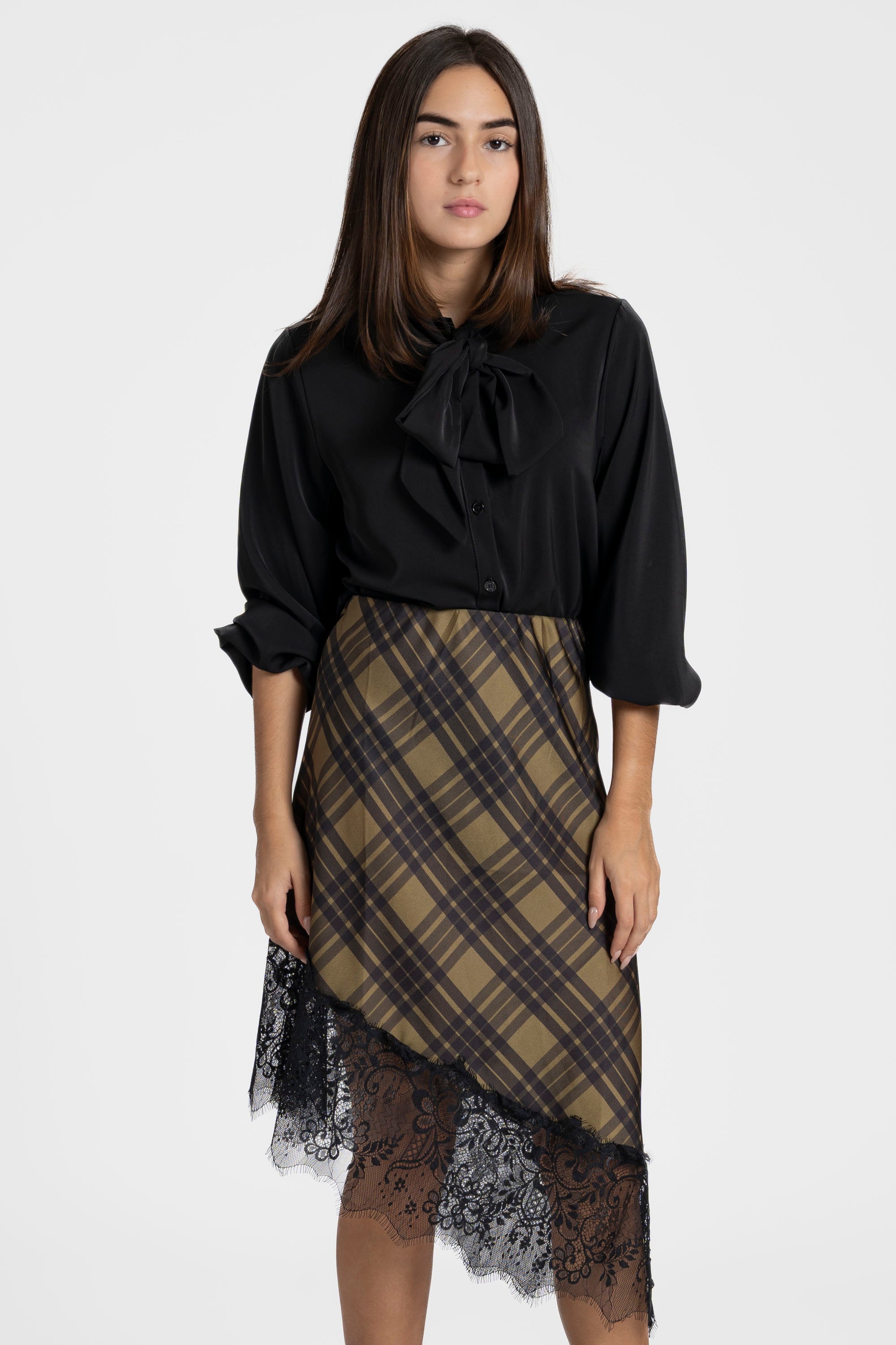 Modèle portant une jupe midi satinée asymétrique en satin avec des empiècements en dentelle, associée à une blouse noire élégante.