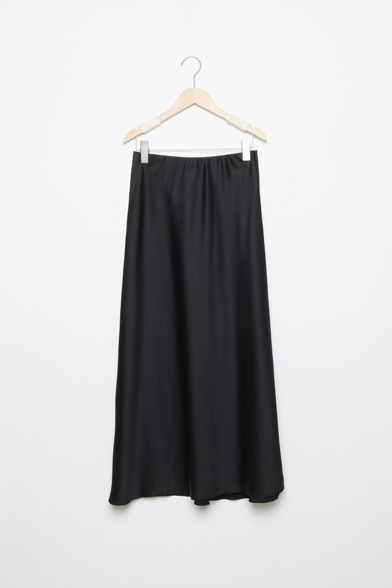 Jupe midi droite satinée noire sur un cintre, montrant la finition soignée en 100% polyester.