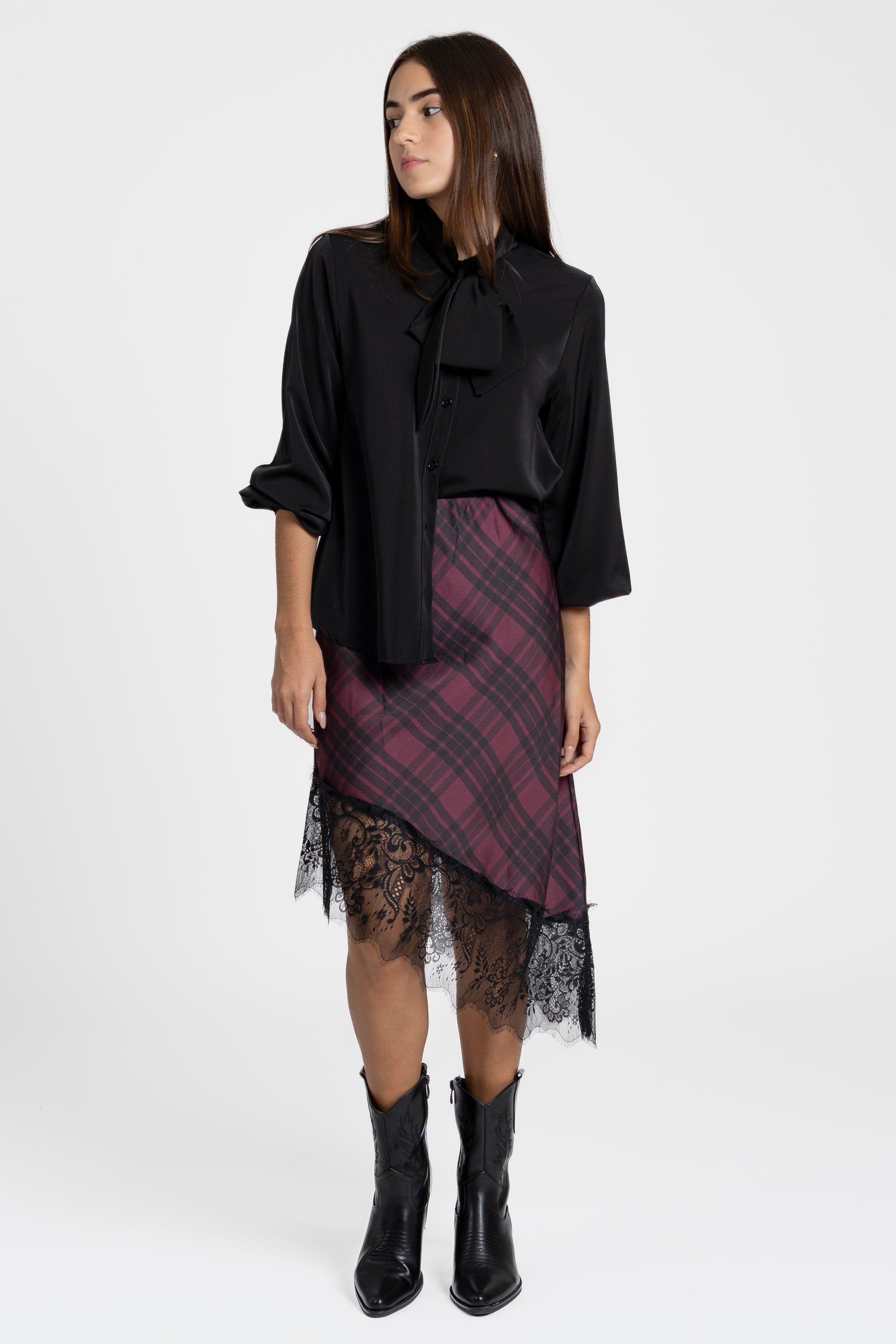 Femme en jupe midi satinée asymétrique en satin rouge prune, accompagnée d'une blouse noire, donnant une allure chic.