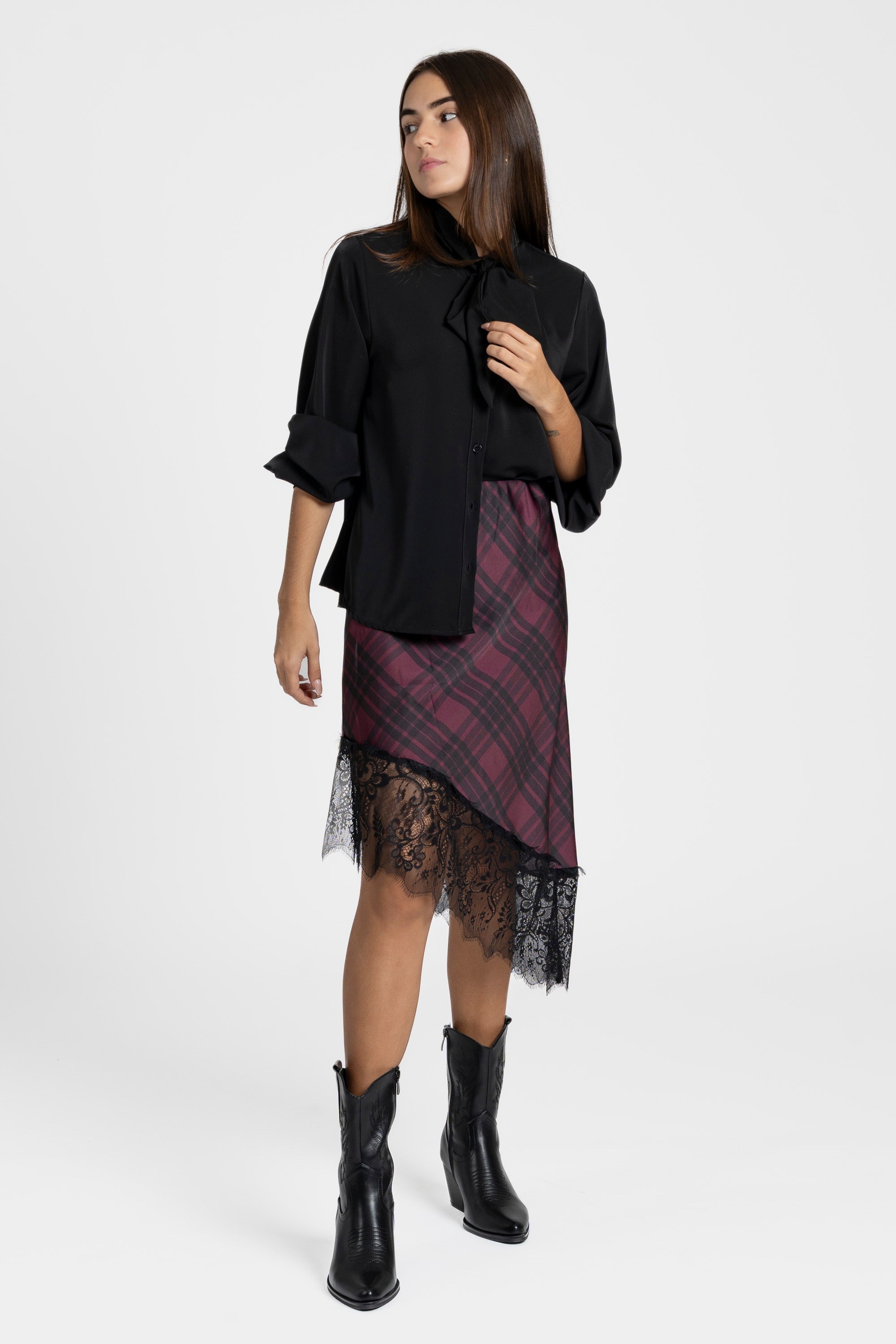 Détail de style d'une jupe midi satinée asymétrique en satin avec dentelle, présentée avec un chemisier noir décontracté.