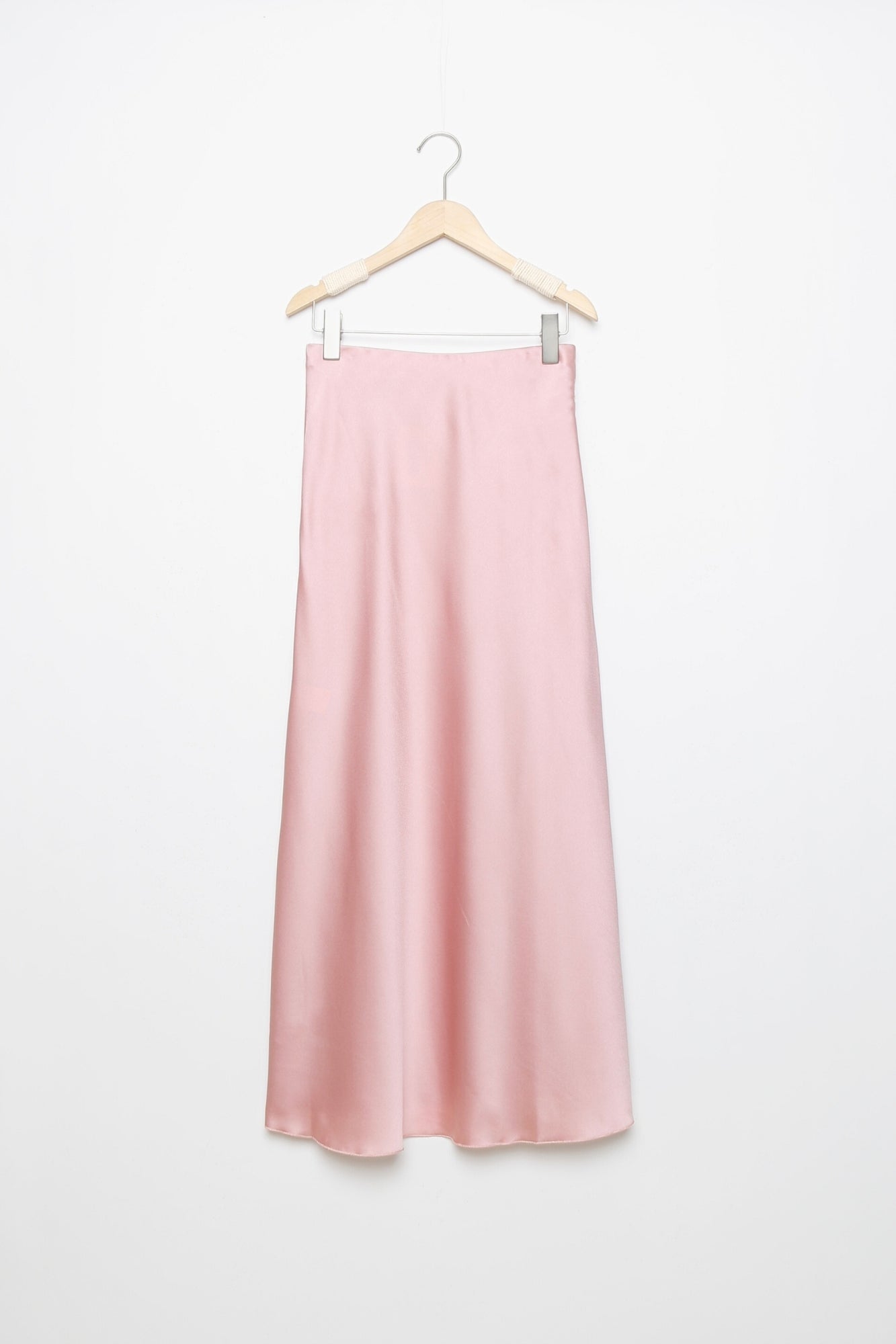 Jupe midi droite satinée en rose pâle, sur un cintre, parfaite pour ajouter une touche de douceur à votre garde-robe.