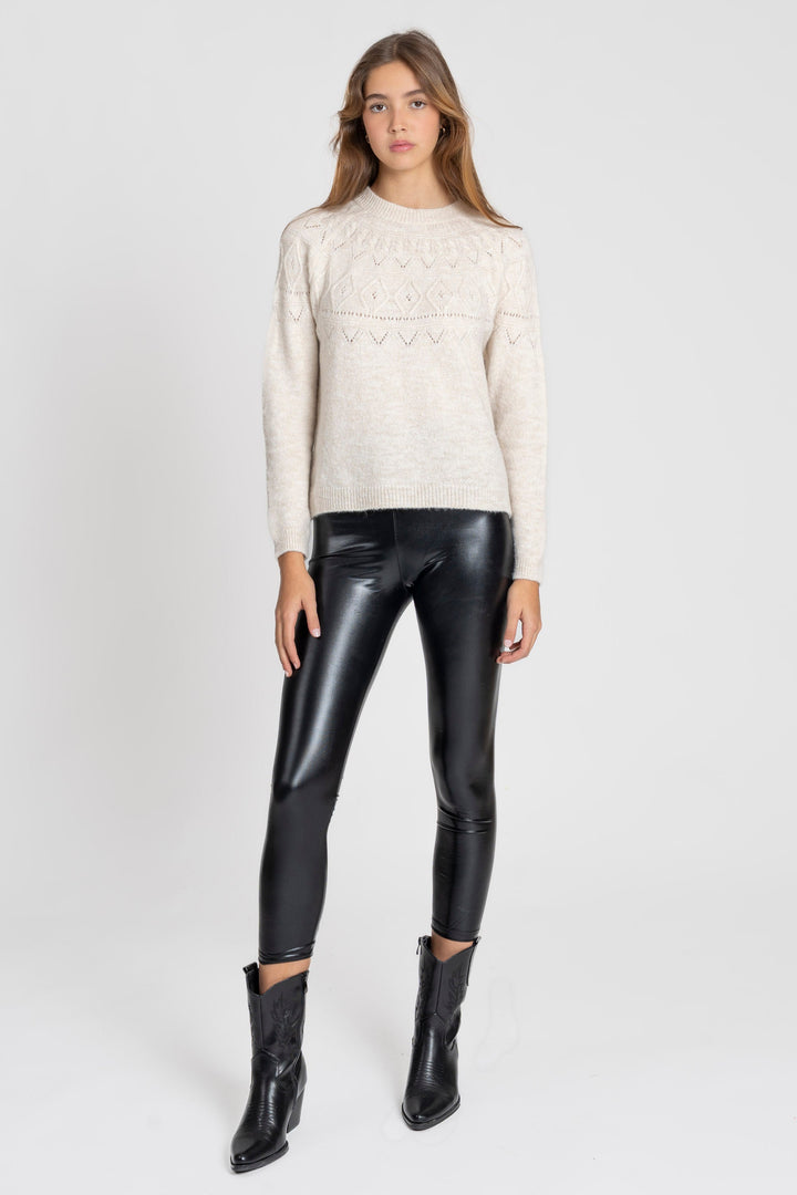 Femme portant un legging noir brillant taille haute, coupe ajustée, avec un pull beige en tricot et des bottes noires.