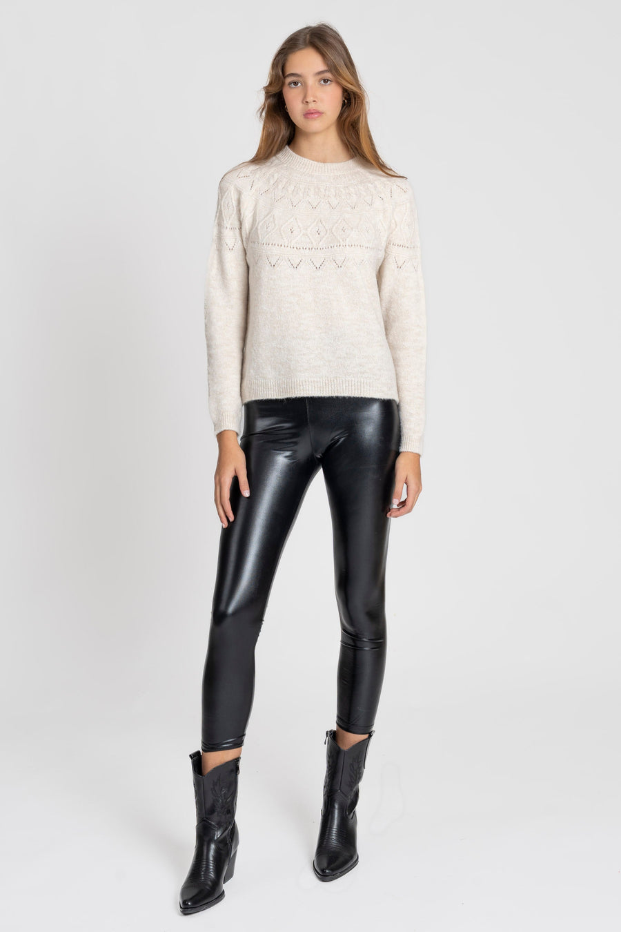 Femme portant un legging noir brillant taille haute, coupe ajustée, avec un pull beige en tricot et des bottes noires.