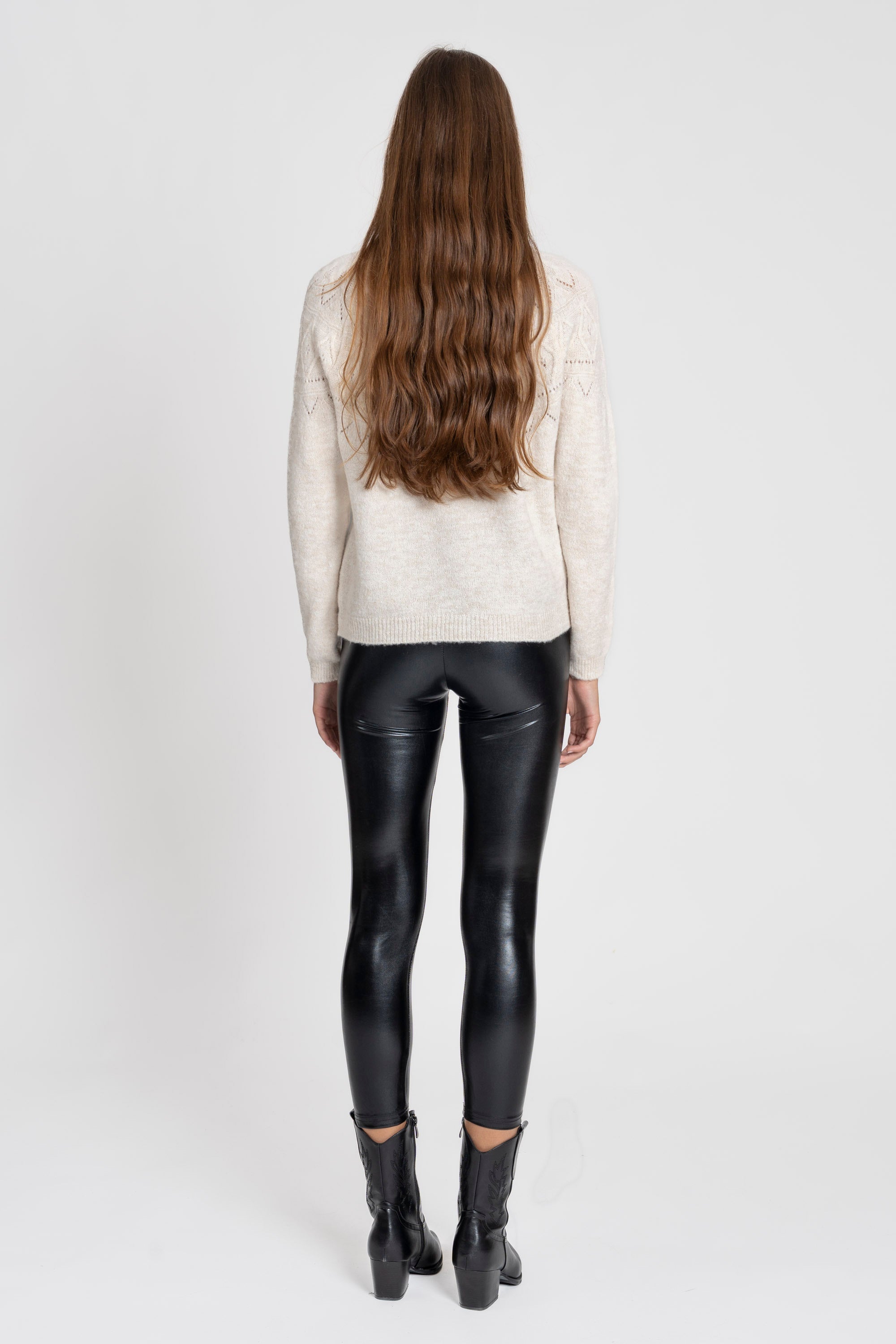 Femme vue de dos en legging noir brillant taille haute, coupe ajustée, avec un pull beige et des bottes noires, mettant en valeur le style du legging.