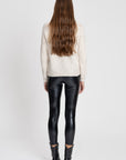 Femme vue de dos en legging noir brillant taille haute, coupe ajustée, avec un pull beige et des bottes noires, mettant en valeur le style du legging.