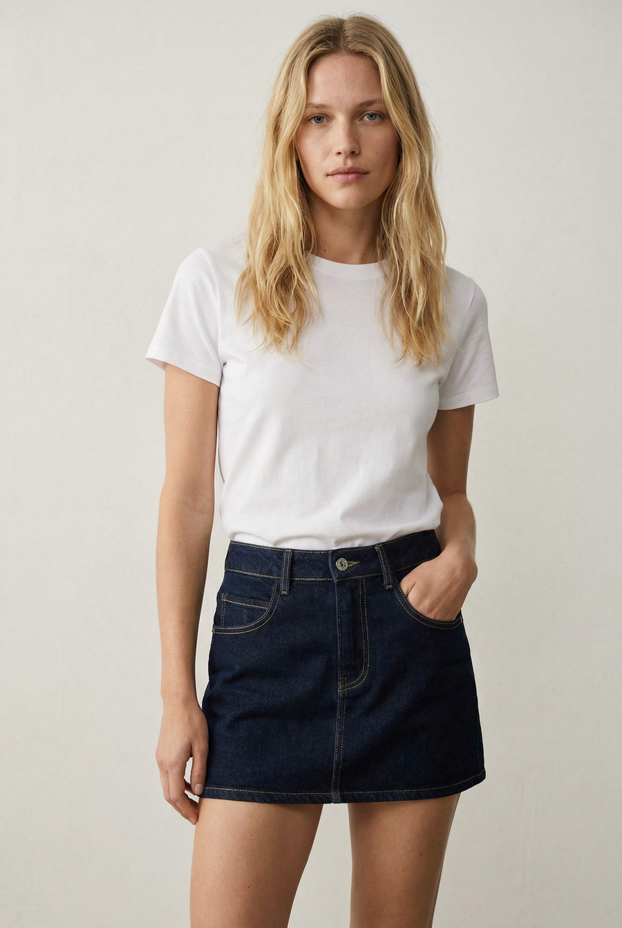 Modèle féminin en mini jupe en jean, style urbain, avec t-shirt blanc dans un décor minimaliste.