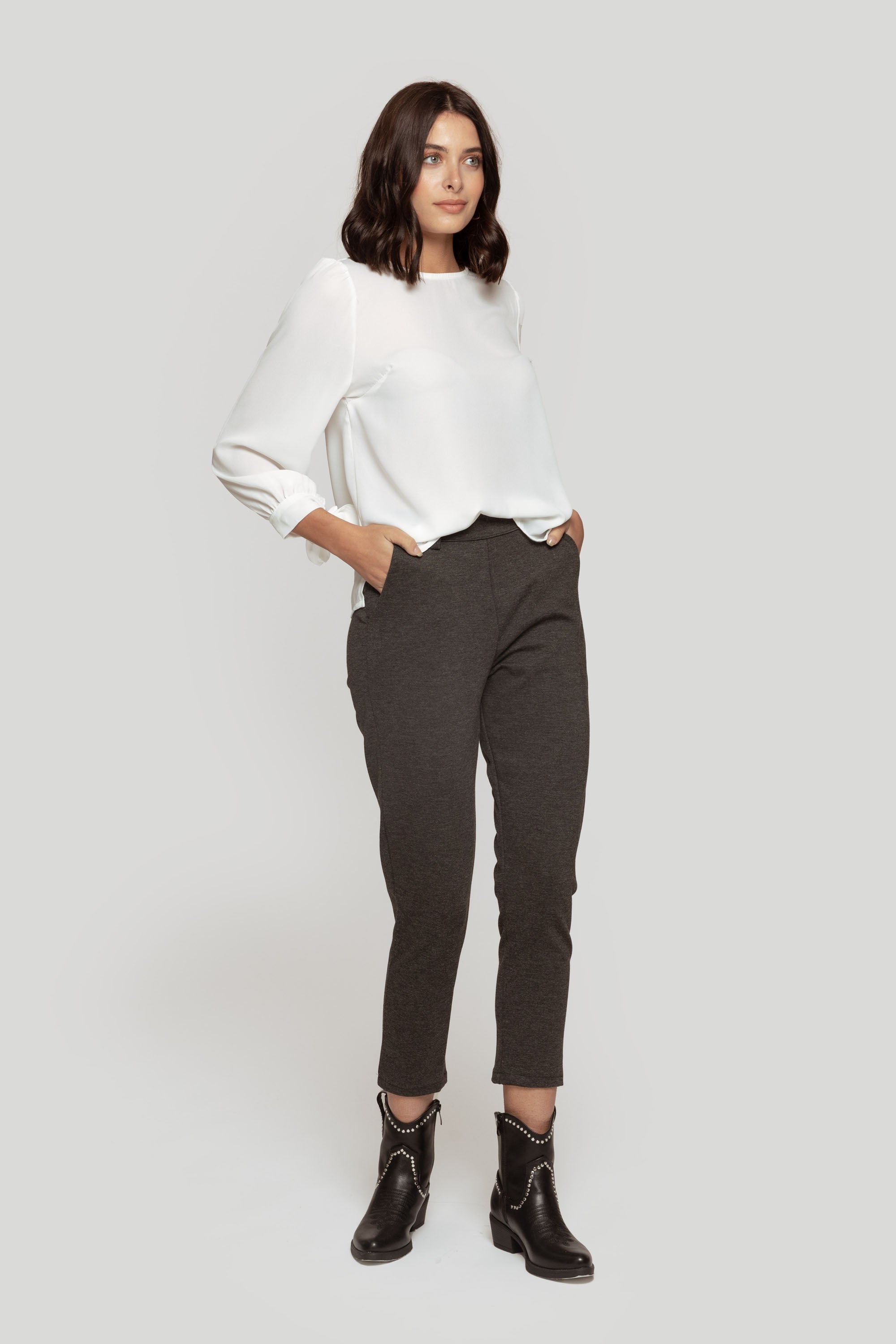 Femme en pantalon fluide taille haute gris, stylée avec un haut blanc, affichant un look contemporain.