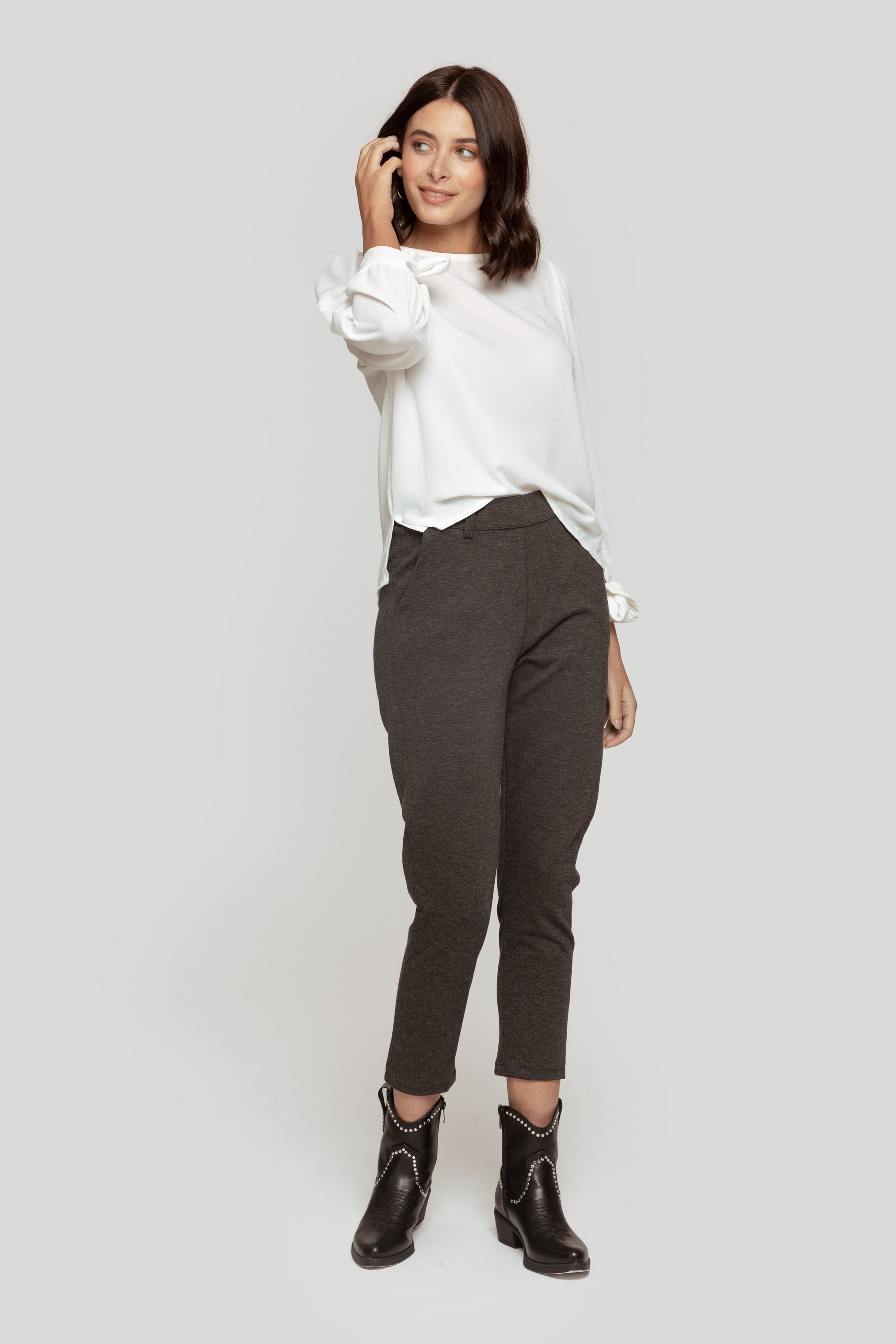 Femme souriante portant un pantalon fluide taille haute gris avec un haut blanc, pour un look décontracté.