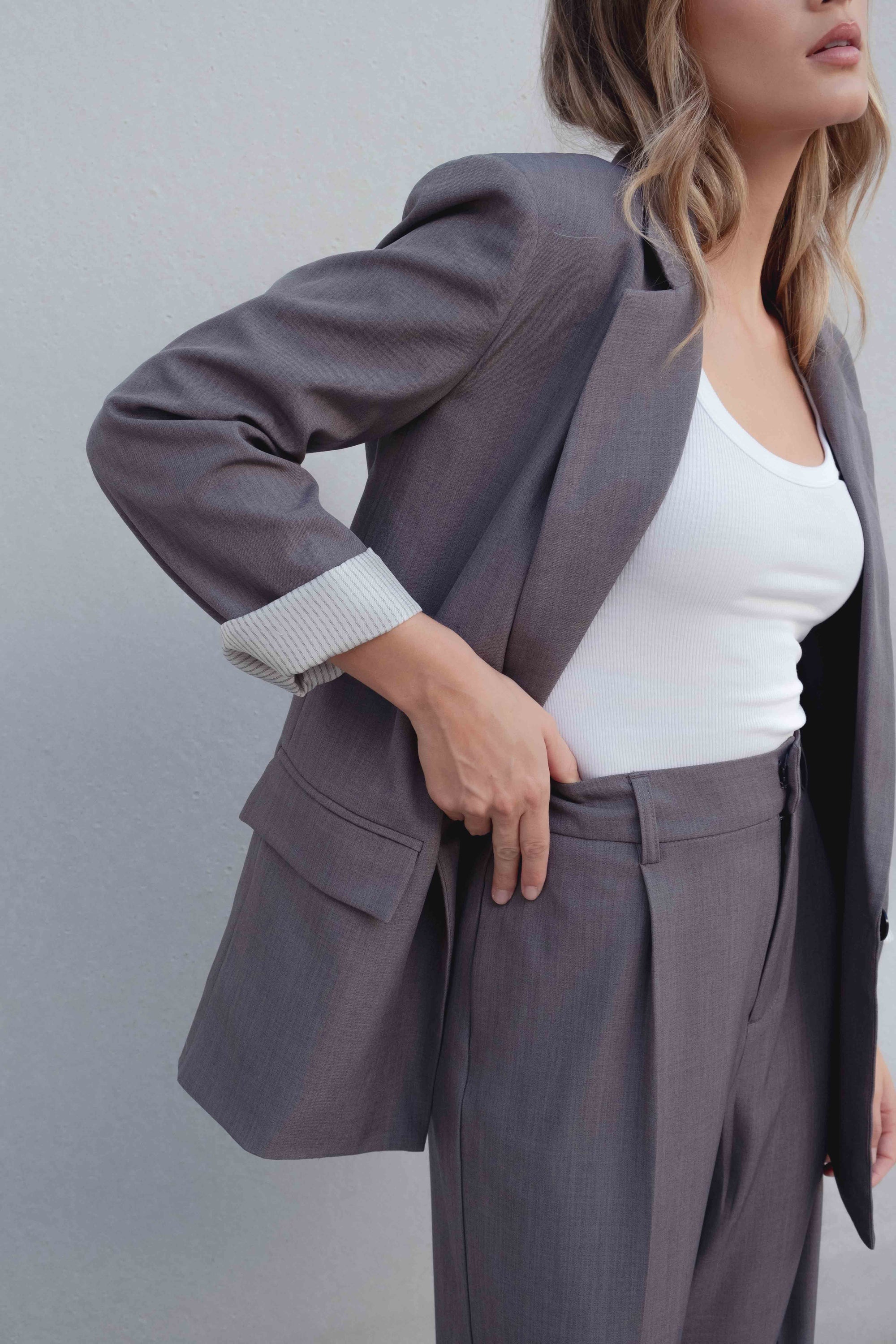 Pantalon Large Taille Haute Gris Élastique Avec Pinces, Look élégant d'une femme portant un blazer et un top blanc, montrant le pantalon qui allonge la silhouette.