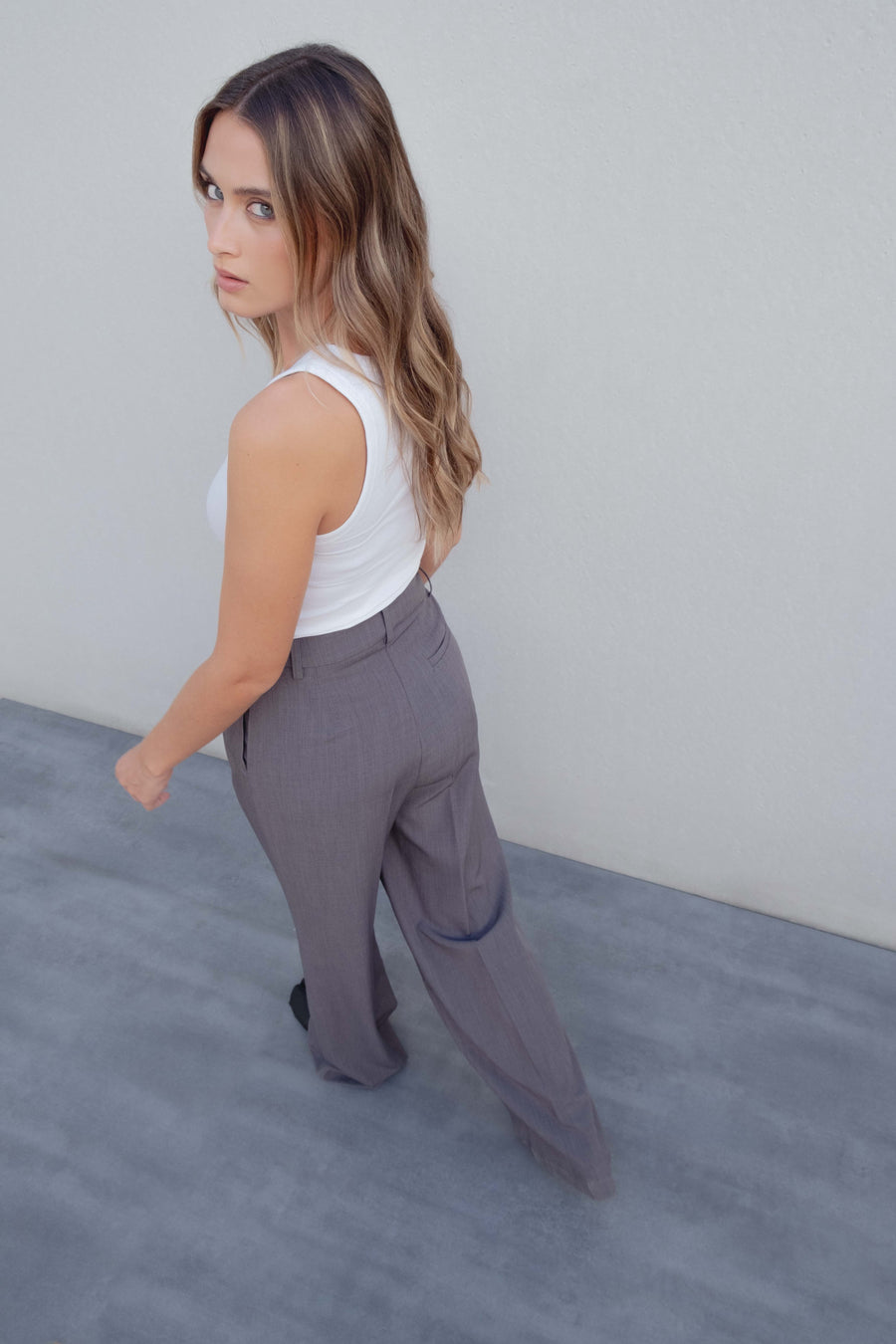 Pantalon Large Taille Haute Gris Élastique Avec Pinces, Femme regardant en arrière tout en portant un top blanc et un pantalon gris, soulignant le style sophistiqué.