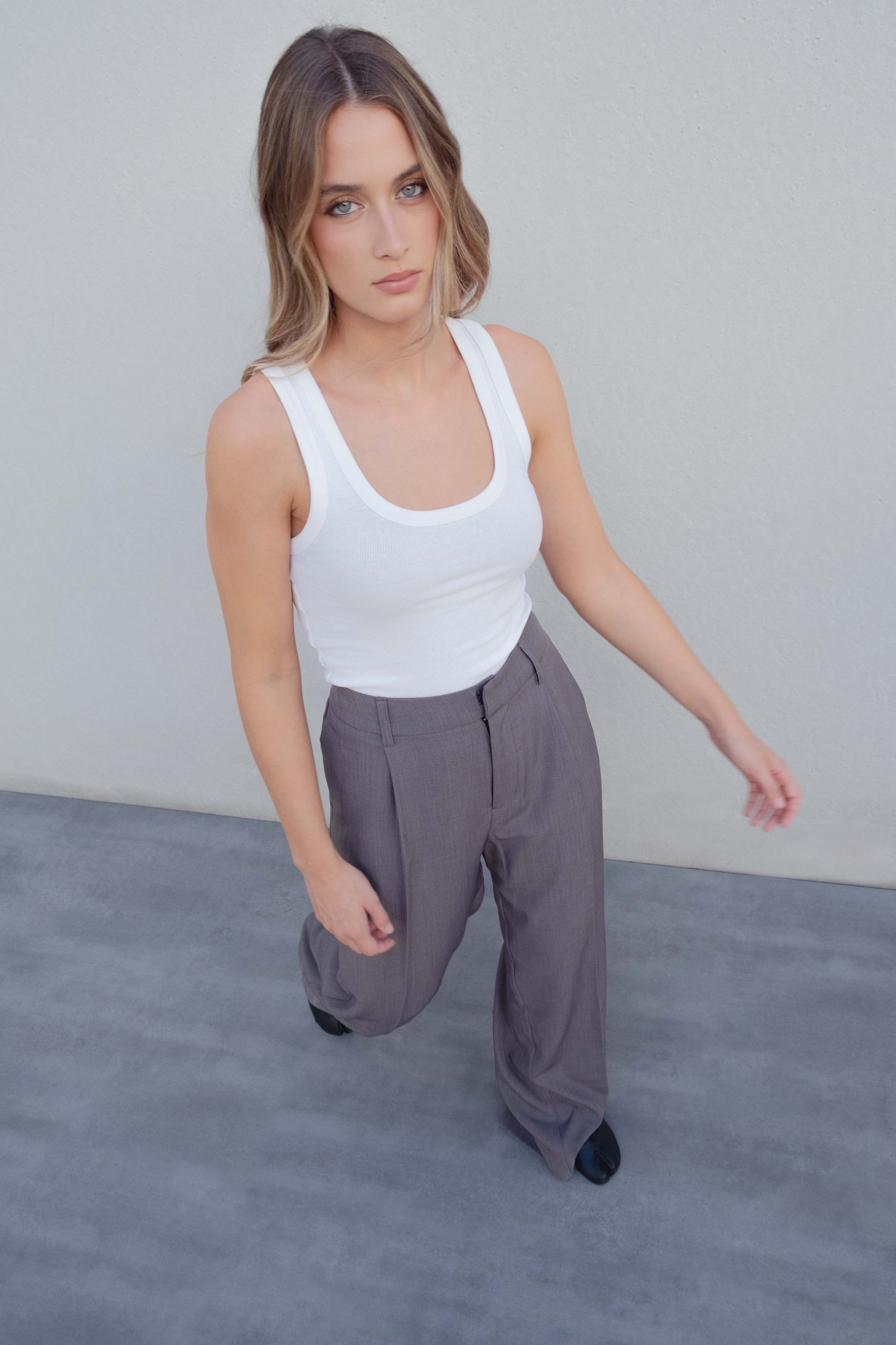 Pantalon Large Taille Haute Gris Élastique Avec Pinces, Femme en top blanc marchant avec confiance dans un pantalon large gris, mettant en avant le confort et l'élégance.