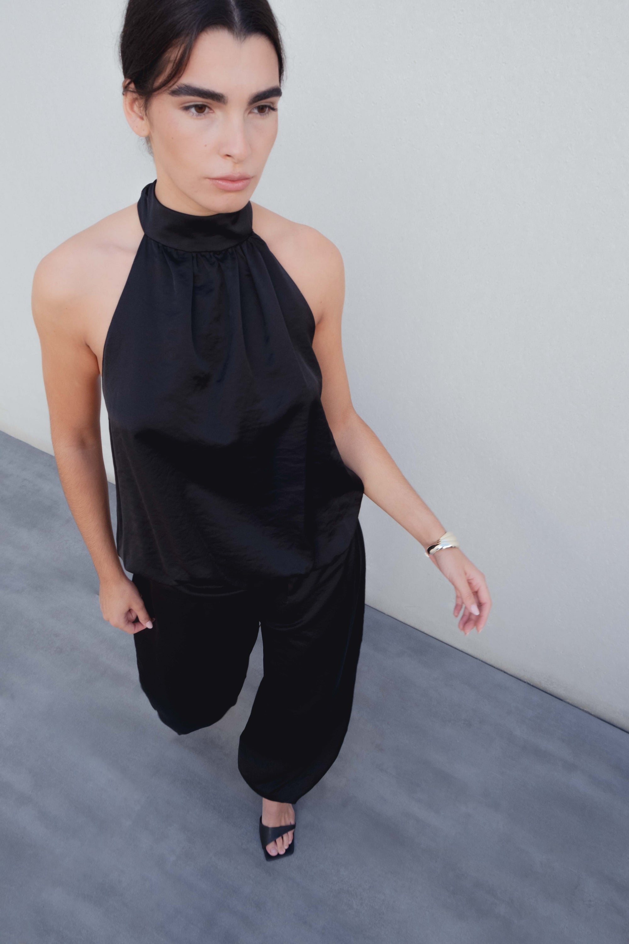 Femme marchant avec confiance dans un pantalon bombacho satiné noir et un haut noir, capturant l'essence d'un style moderne et chic.