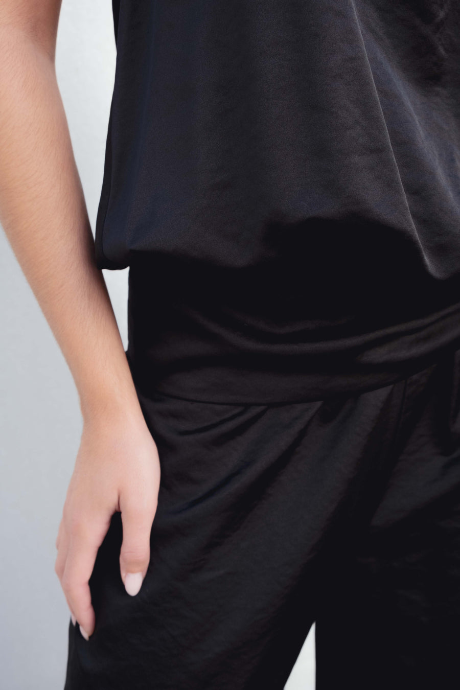 Zoom sur le pantalon bombacho satiné noir porté par une femme, mettant en avant la texture satinée et la taille élastique pour un confort optimal.