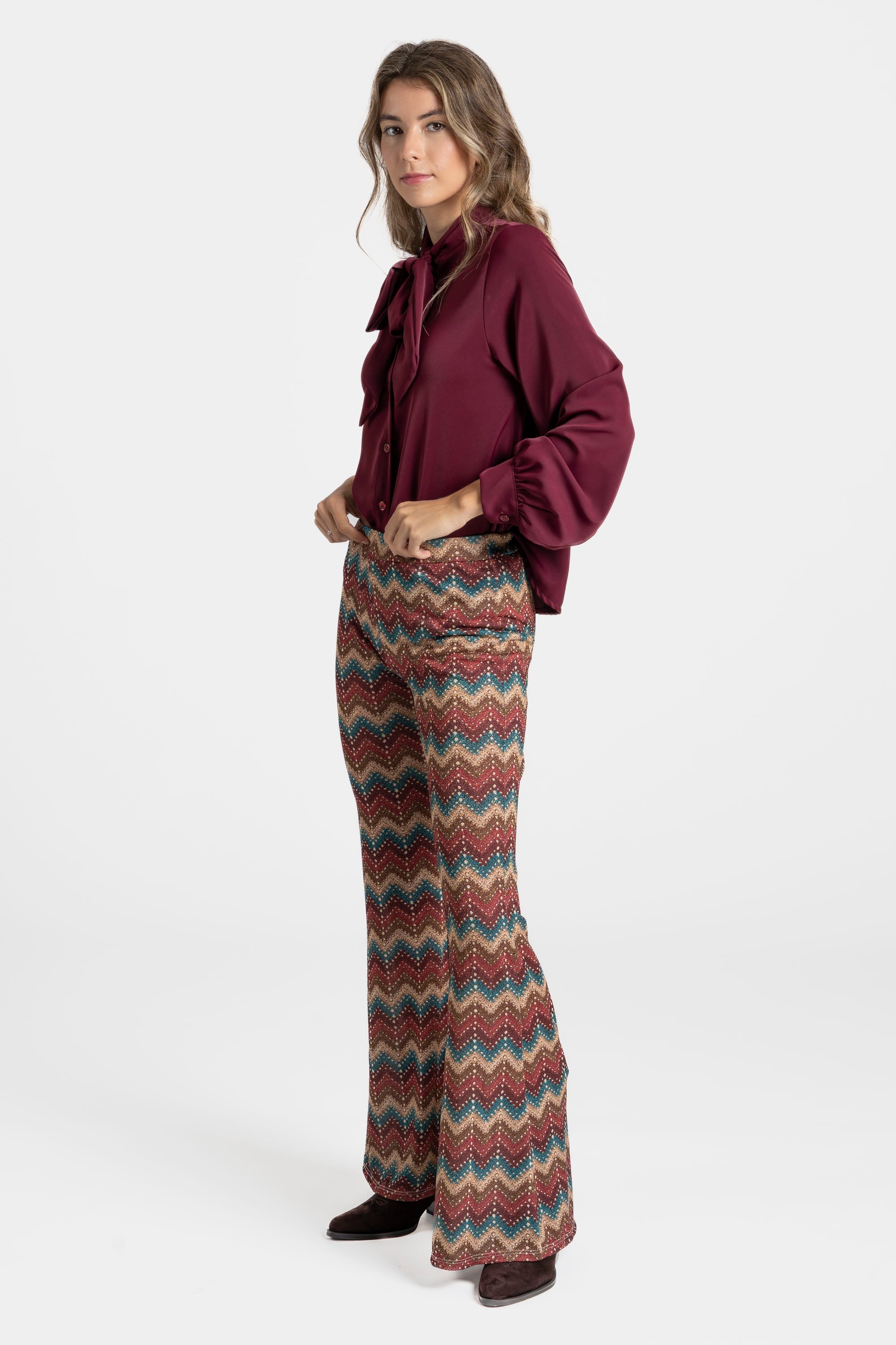 Femme élégante dont le pantalon flare taille haute fluide imprimé en zigzag multicolore vient compléter une blouse bordeaux.