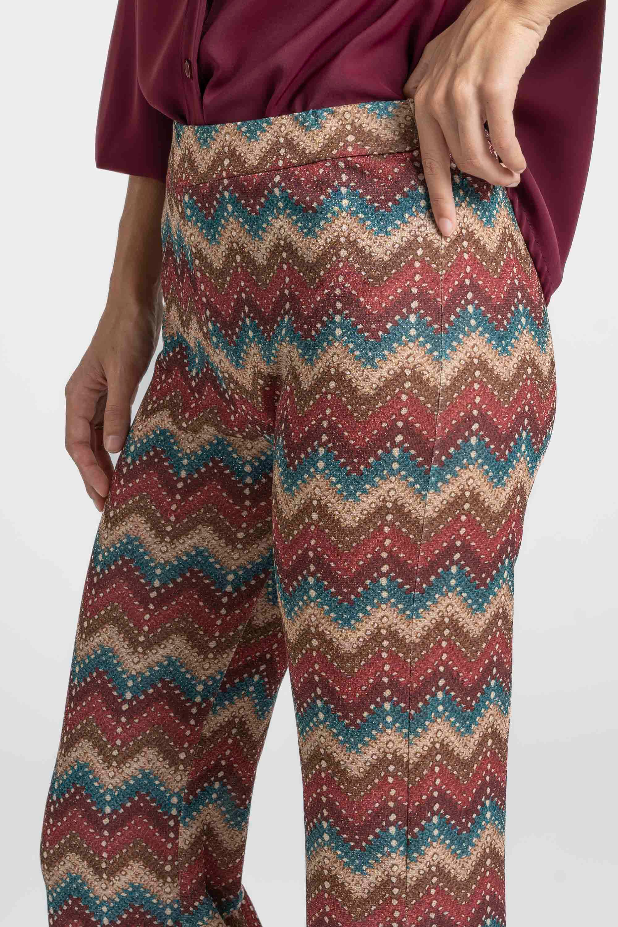 Gros plan sur le pantalon flare taille haute fluide imprimé en zigzag multicolore porté par une femme.