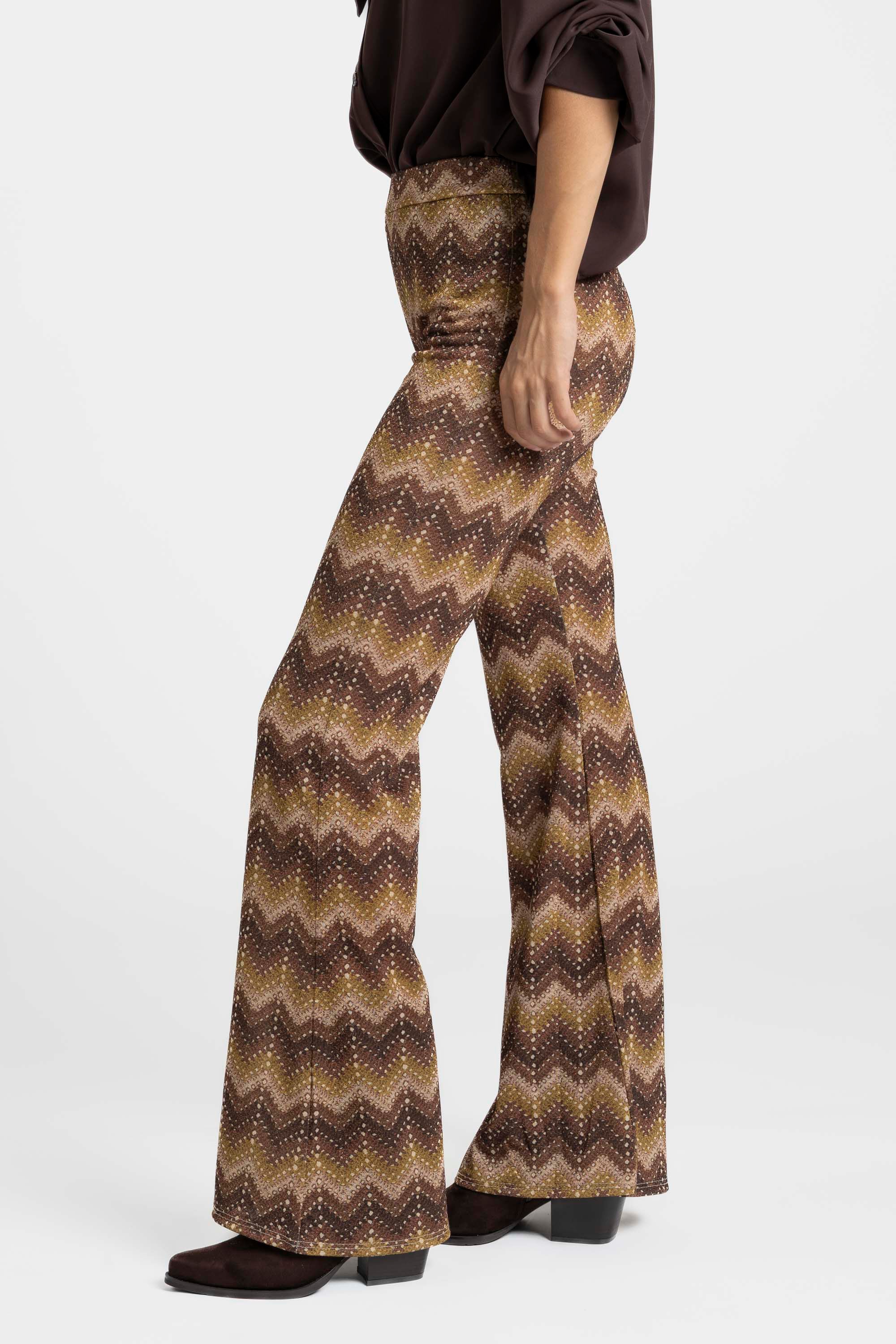 Profil d'une femme avec un pantalon flare taille haute fluide imprimé en zigzag marron et une blouse assortie.