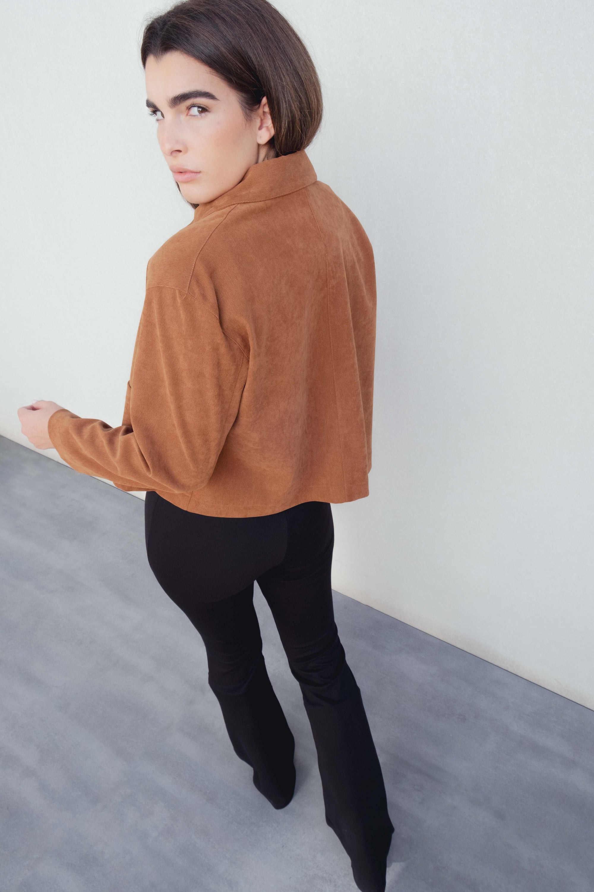 Femme portant un pantalon flare taille haute noir texturé en viscose extensible, avec une veste en suédine marron, vue de dos.
