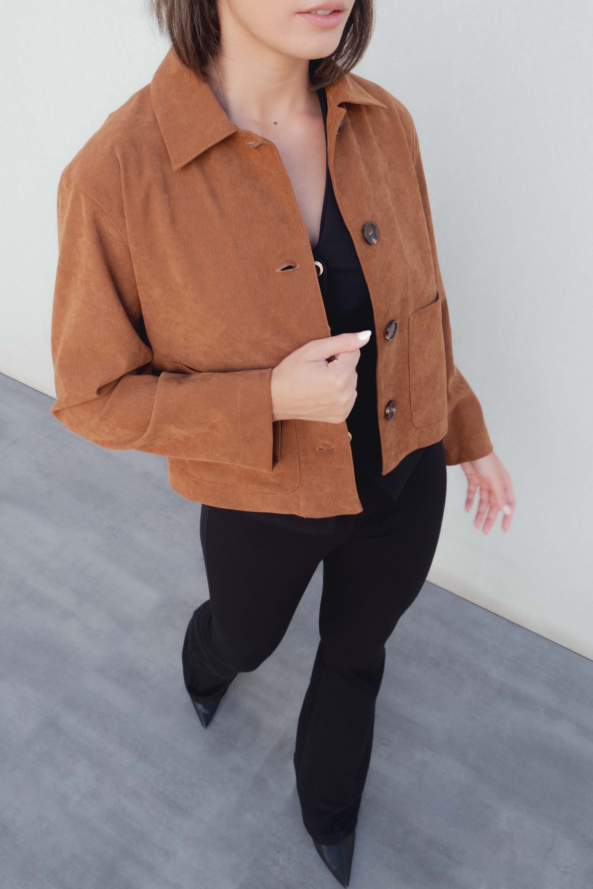 Femme marchant avec un pantalon flare taille haute noir texturé en viscose extensible, associée à une veste en suédine marron.