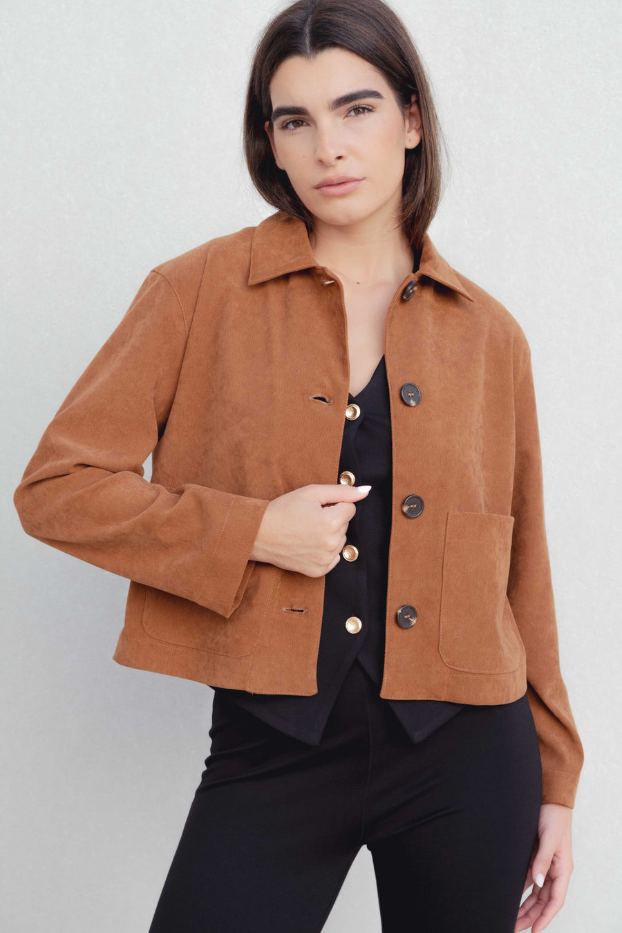 Femme posant avec un pantalon flare taille haute noir texturé en viscose extensible et une veste en suédine marron, mettant en avant une style décontracté.