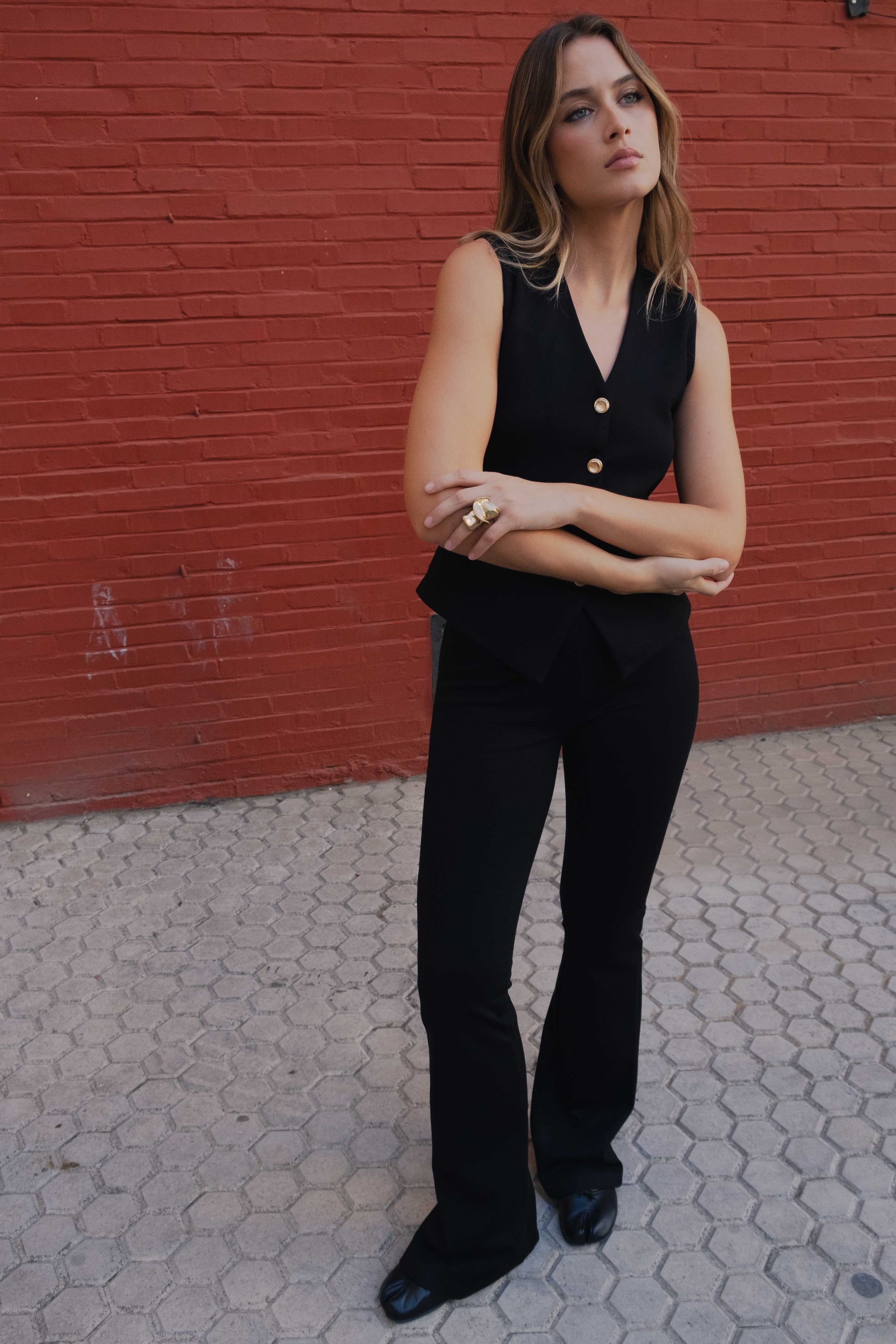 Femme avec un pantalon flare taille haute noir texturé en viscose extensible, posant de manière confiante devant un mur rouge.