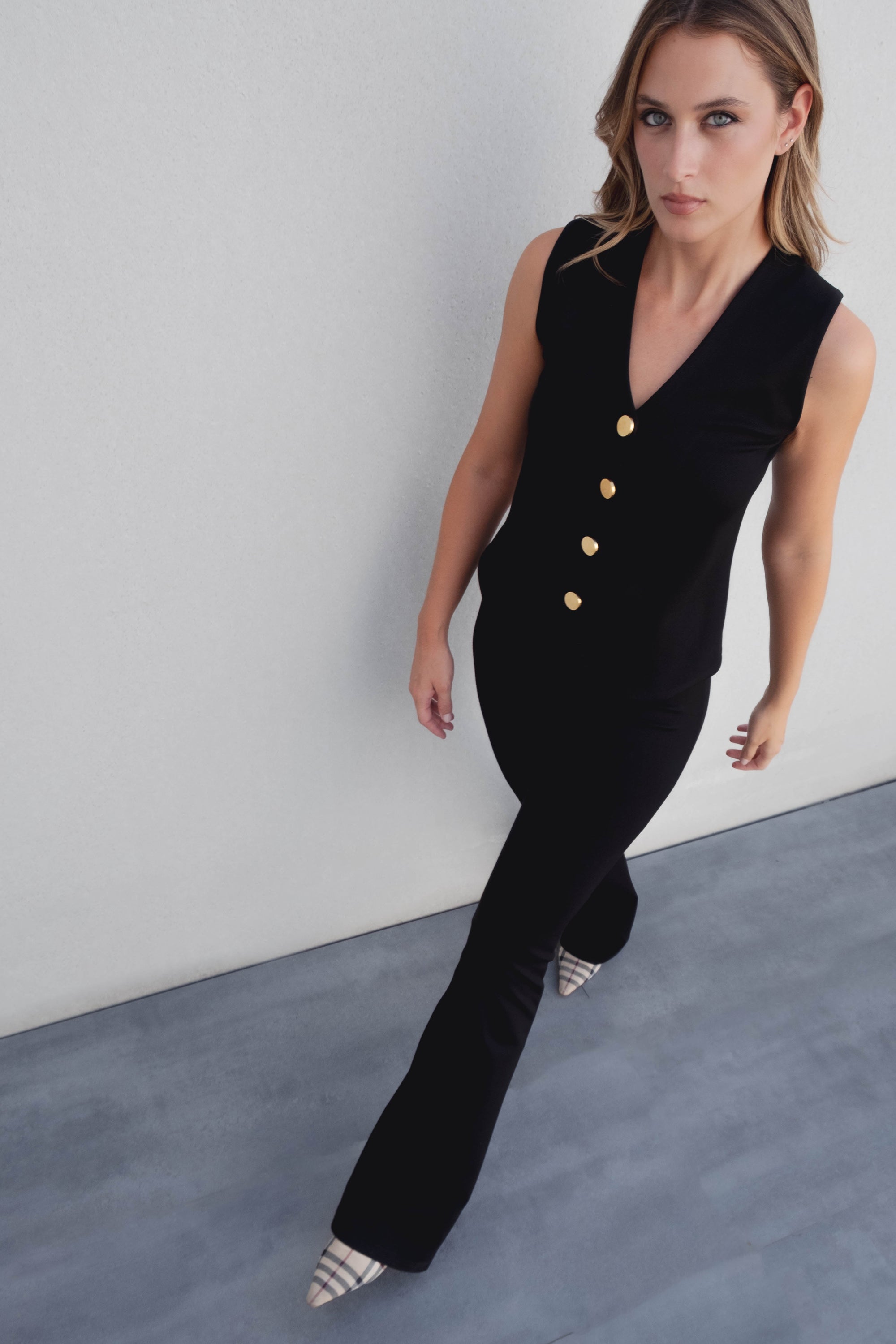 Femme marchant élégamment dans un pantalon flare taille haute noir texturé en viscose extensible, accompagnée d'un haut noir avec des boutons dorés.