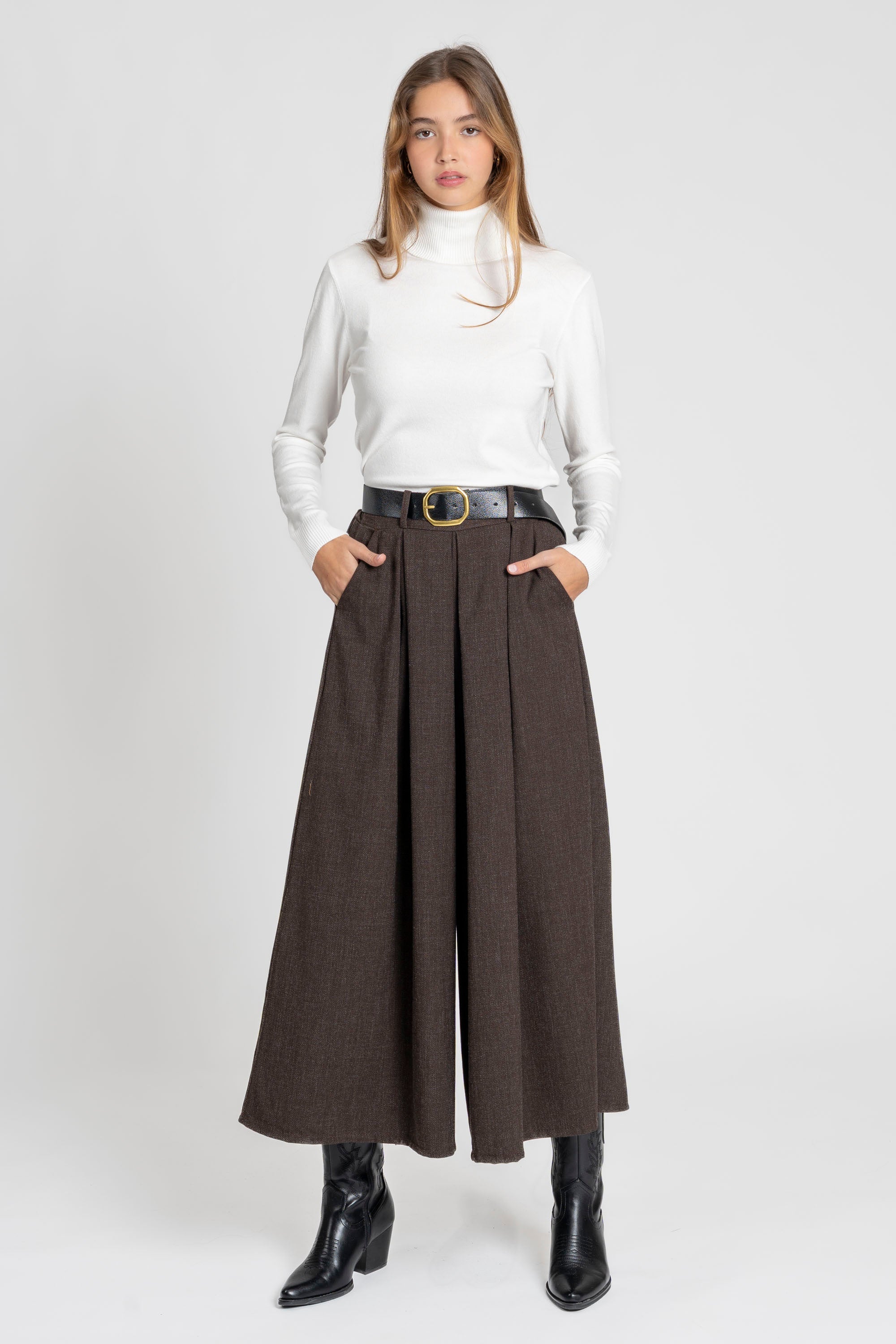 Femme portant un pantalon large taille haute pour femme, coupe fluide midi et ceinture intégrée, avec un haut blanc et des bottes noires.
