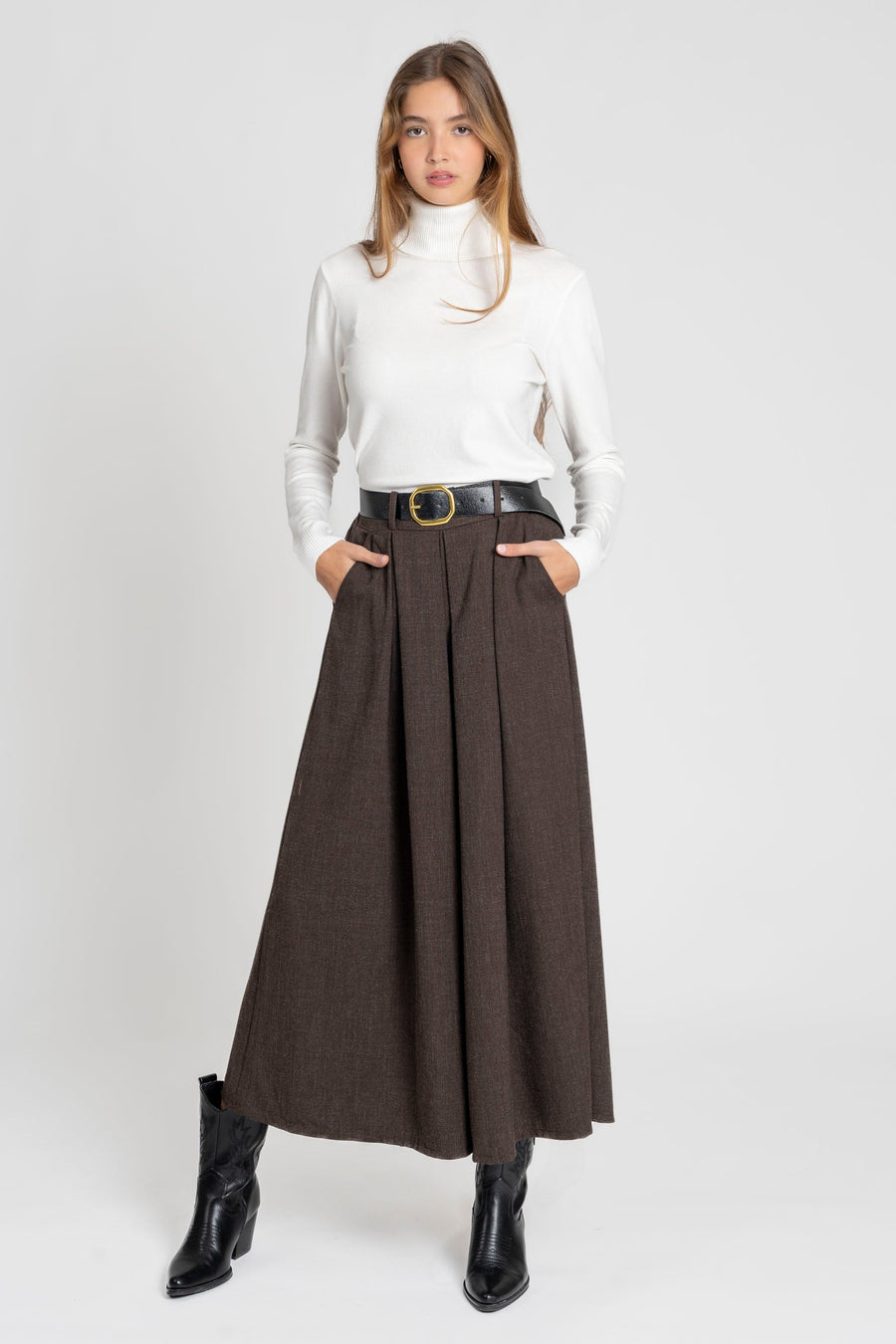 Femme debout mettant en avant un pantalon large taille haute femme en tissu fluide, avec un haut blanc et des bottes noires.
