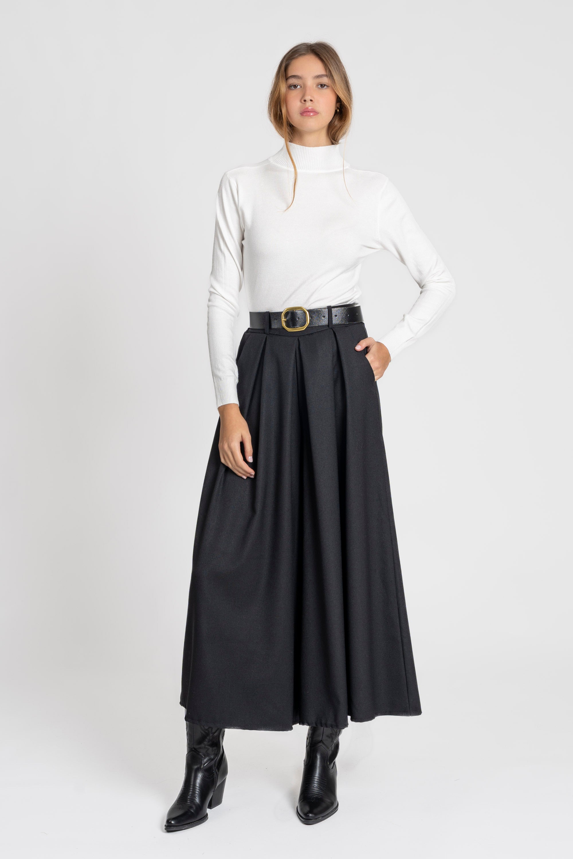 Femme portant un pantalon large taille haute femme en noir, associé à un haut blanc et des bottes.