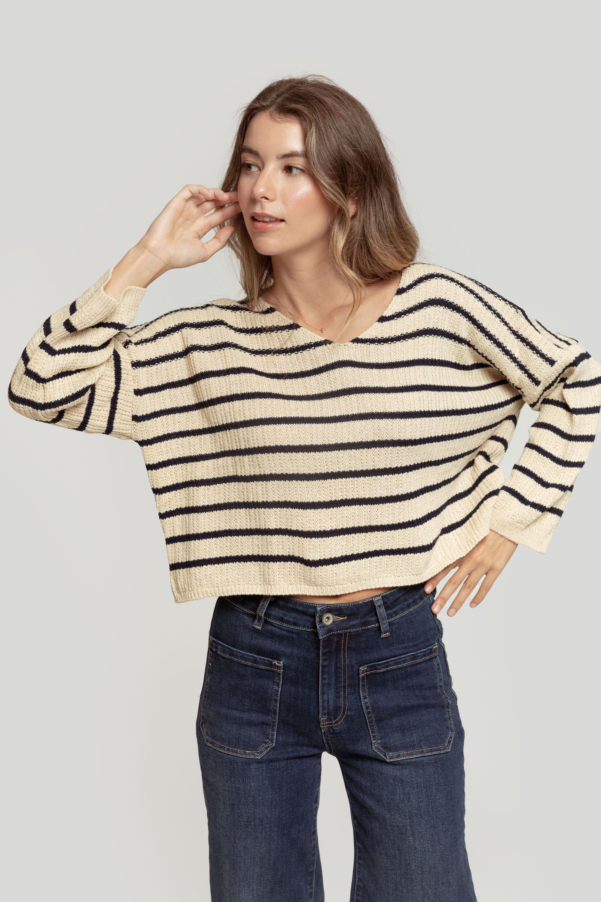 Modèle féminin dans un pull court femme en maille torsadée col V style cropped, avec des rayures bleu marine sur fond crème.