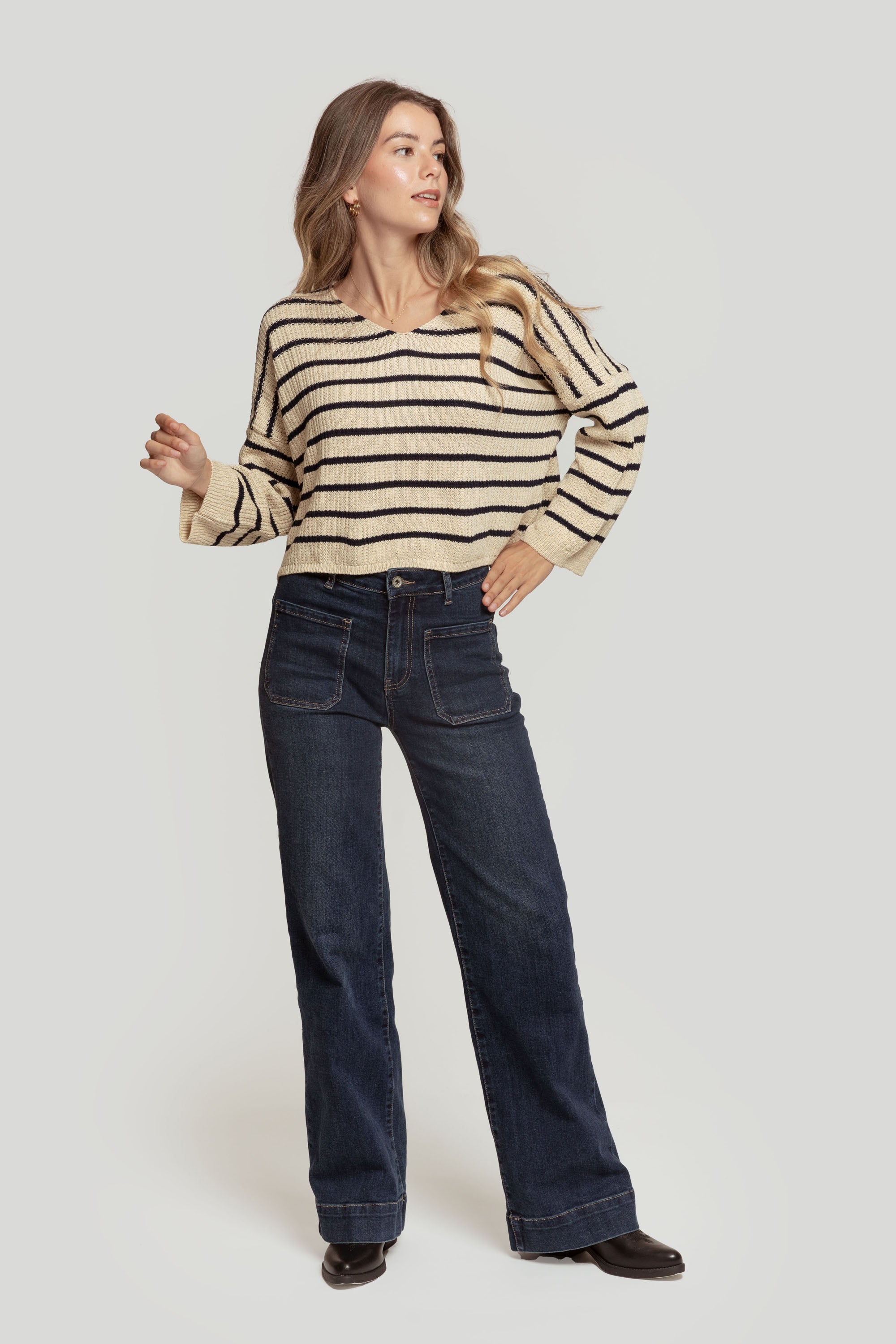 Vue latérale d'une femme portant un pull court femme en maille torsadée col V style cropped avec jeans foncés.
