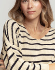 Gros plan sur une modèle souriante dans un pull court femme en maille torsadée col V style cropped avec des rayures noir et crème.