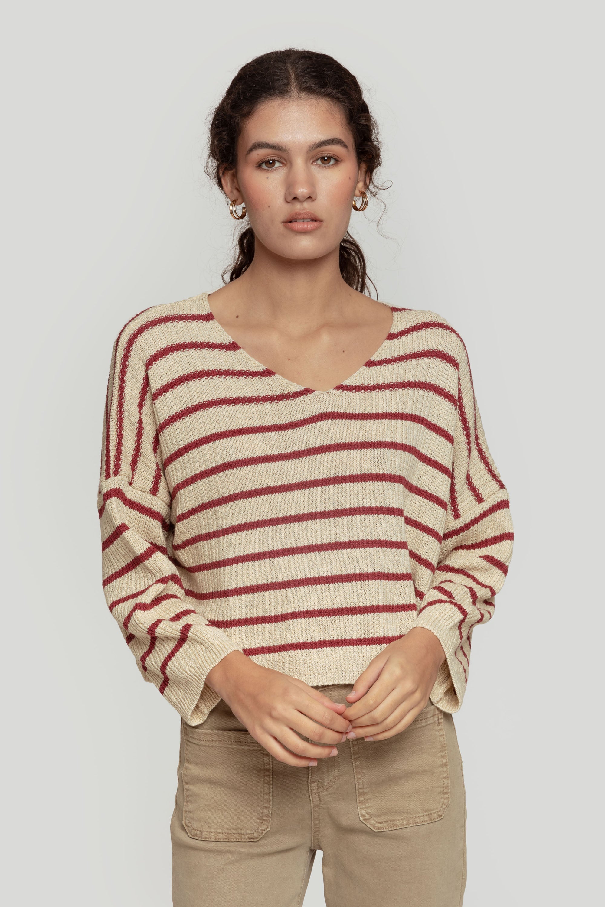 Modèle portant un pull court femme en maille torsadée col V style cropped avec des rayures bordeaux et crème.