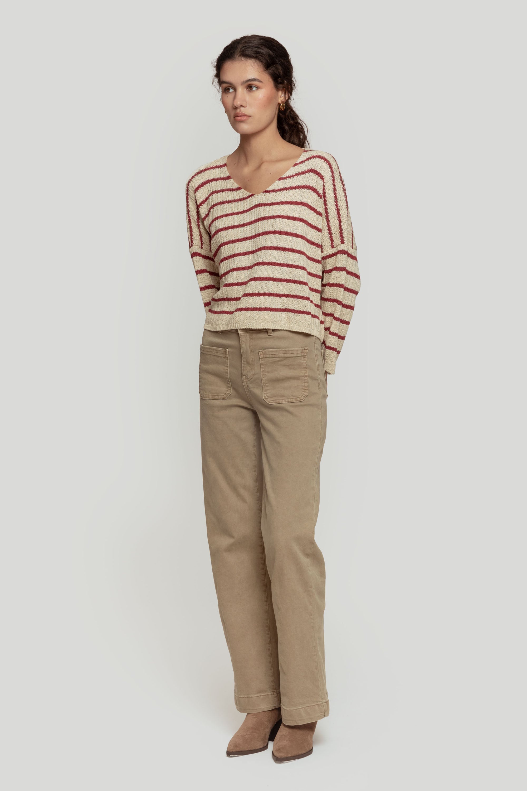 Vue latérale d'un pull court femme en maille torsadée col V style cropped, associé à un pantalon beige.