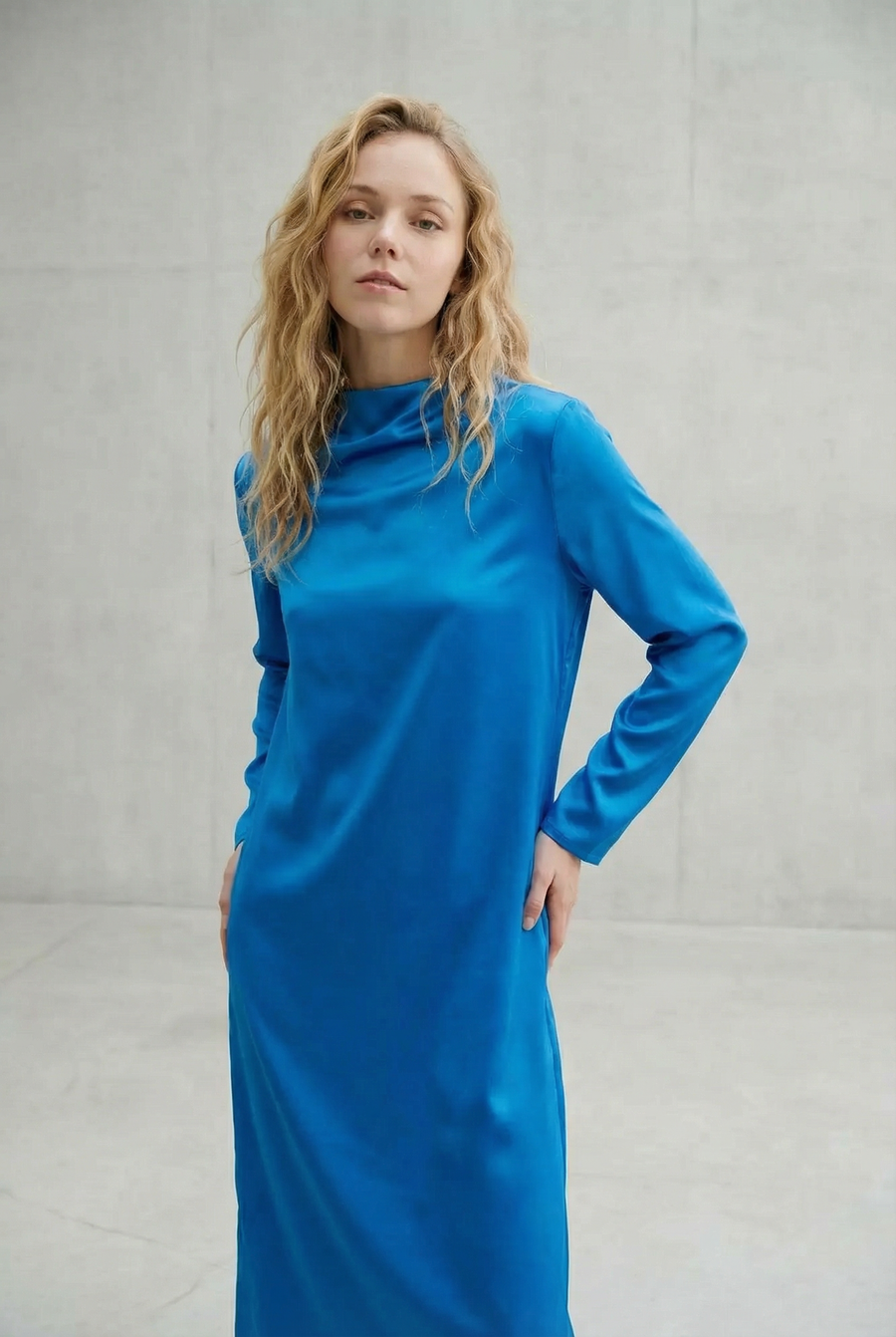 Vestido largo de satén azul eléctrico con cuello alto, mangas largas y abertura en la espalda, elegante y moderno.