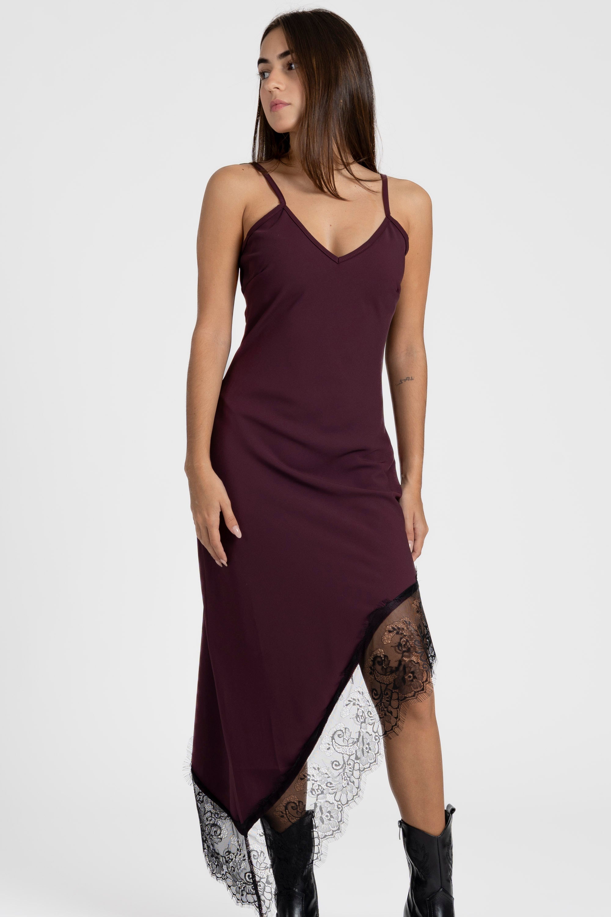 Femme dans une robe asymétrique dentelle Bretelles fines Tissu extensible en bordeaux, soulignant l'asymétrie et le style moderne.